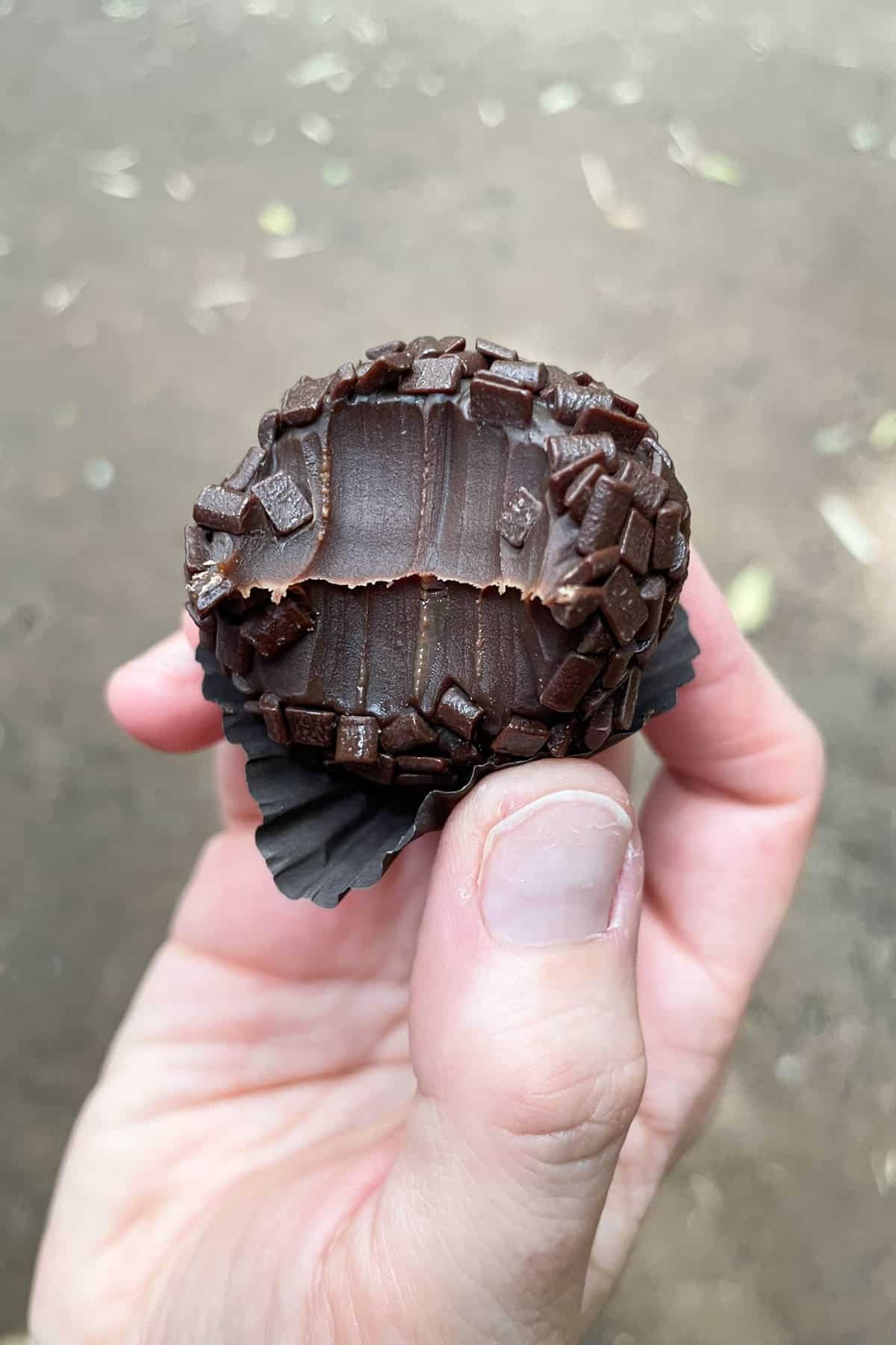 A hand holding a Brazilian brigadeiro with a bite taken out of it.