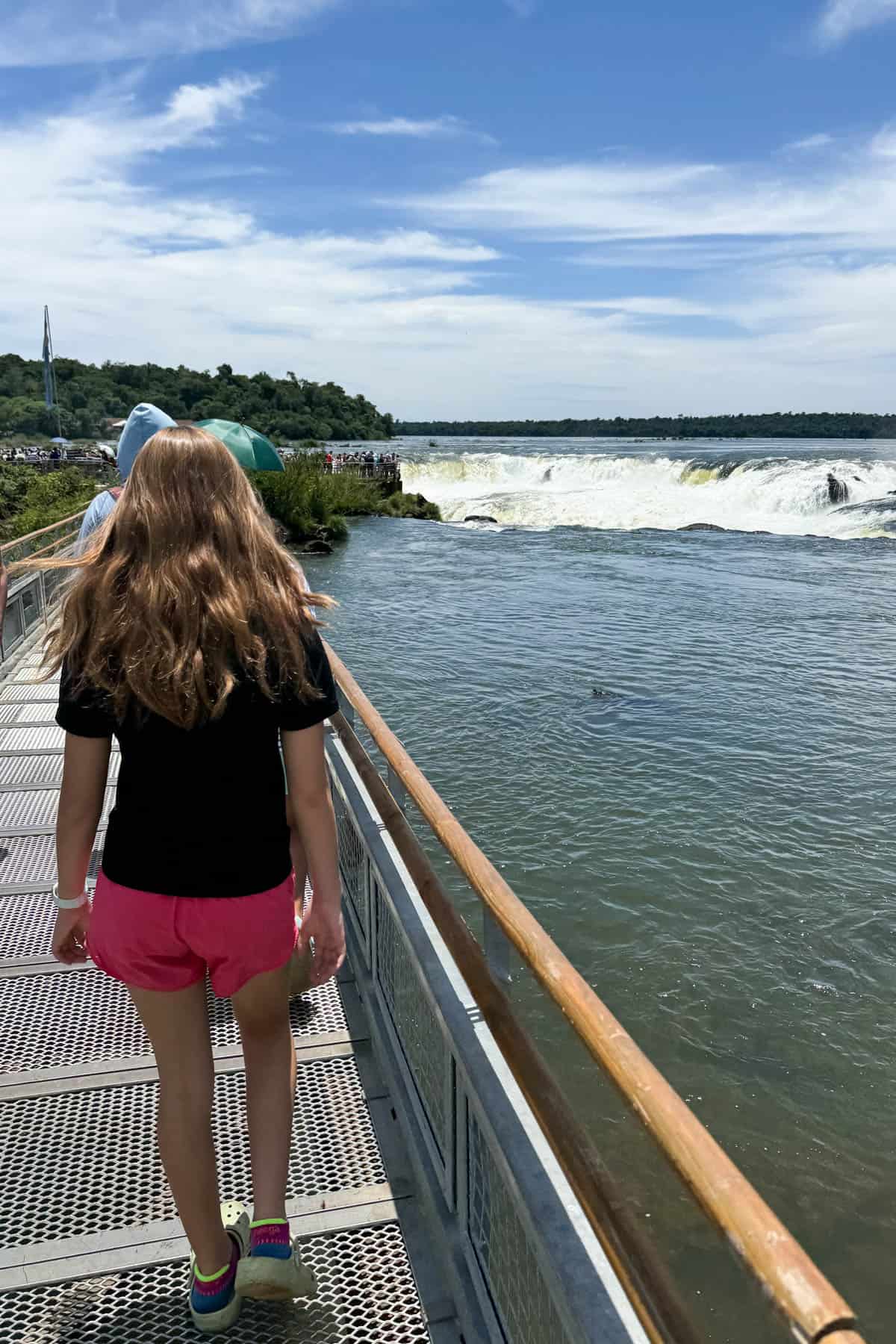 A girl walking along a boardwalk to the top of the Argentina side of Igauzu Falls.
