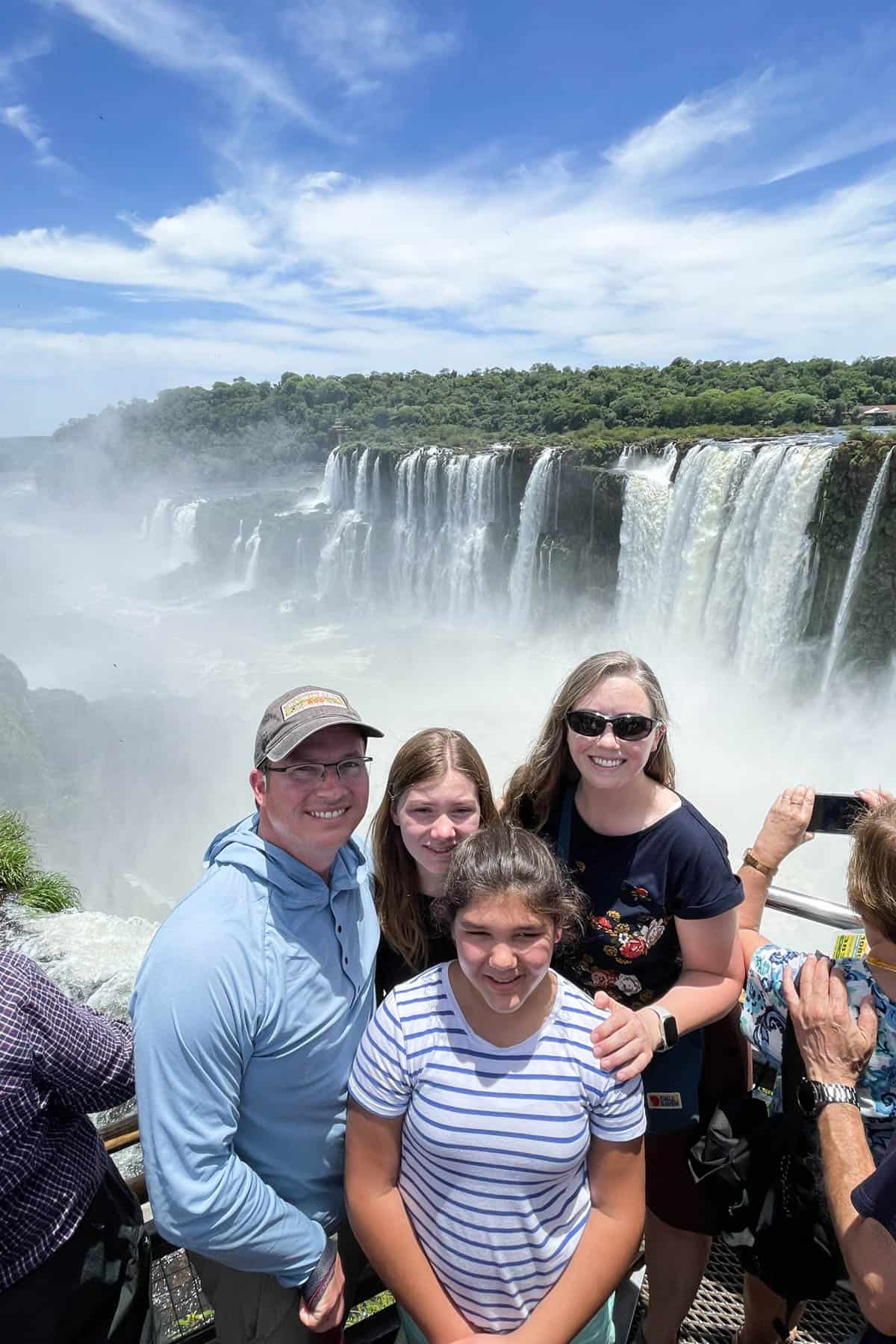 A family of four at Iguazu Falls in Argentina with the Brazil side of the falls behind them.