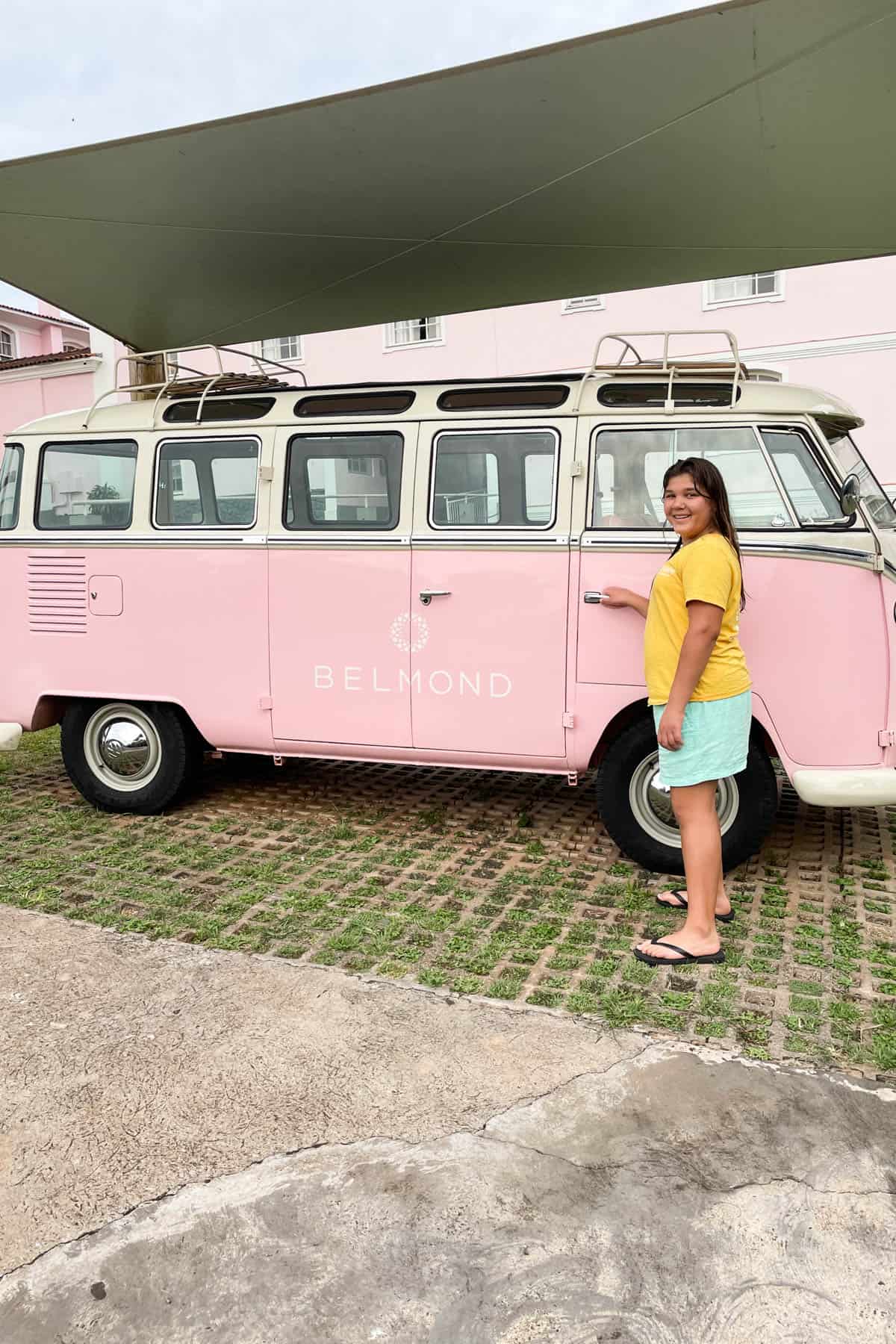 A girl holding the door handle to a pink VW van.