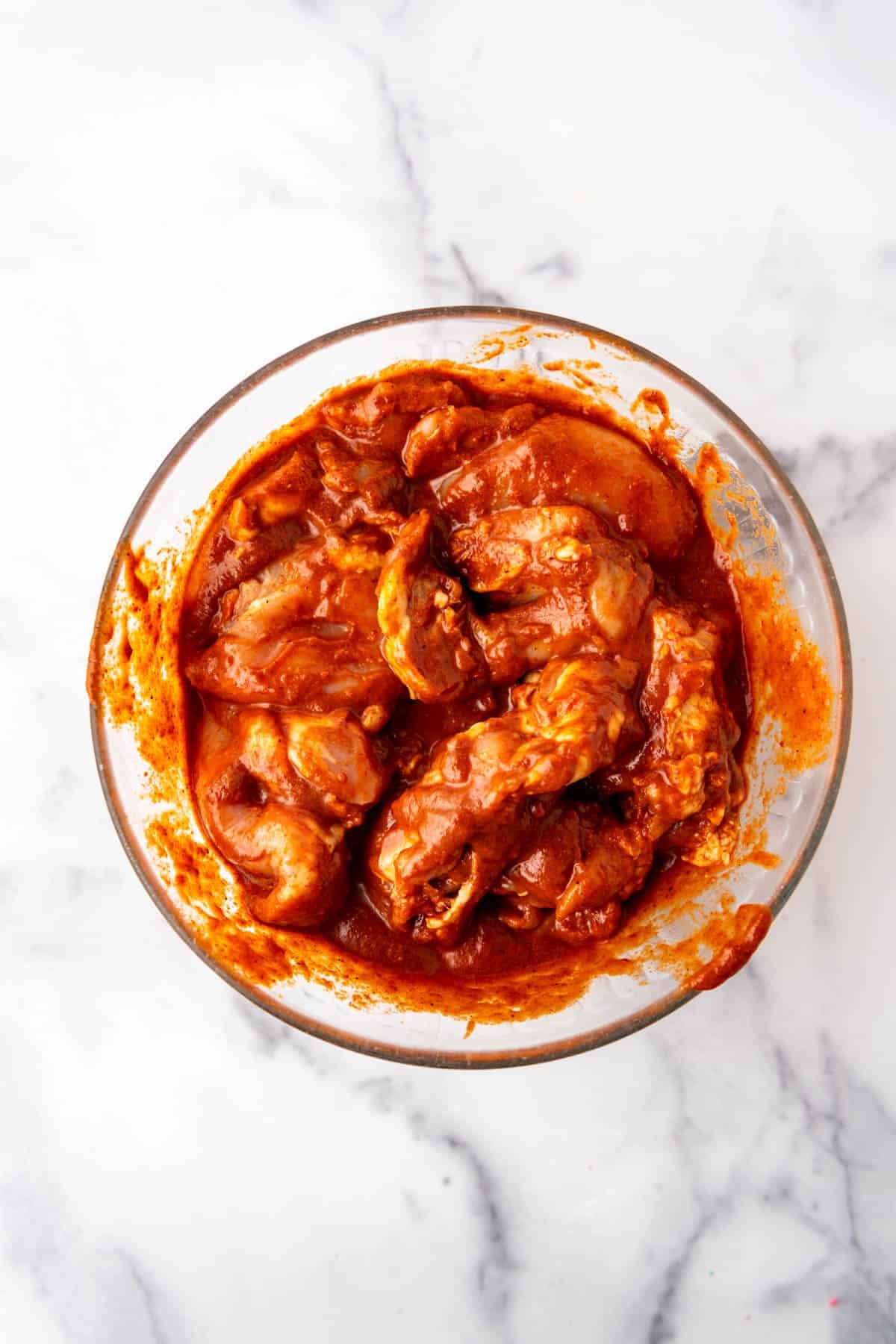 Chicken marinating in a red sauce on a bowl.