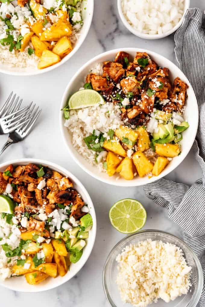 Two chicken al pastor bowls with queso fresco and limes nearby.