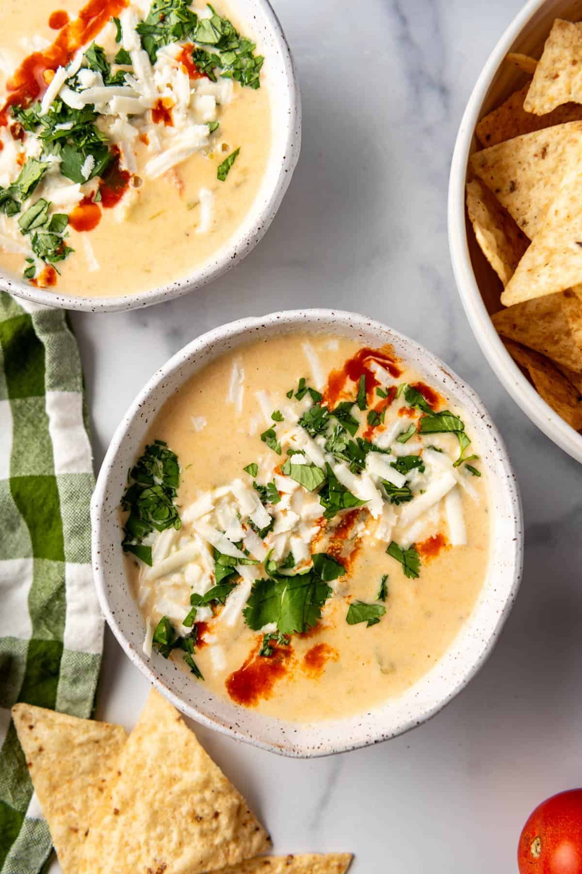 An overhead image of a bowl of queso topped with cotija cheese, chopped cilantro, and hot sauce.