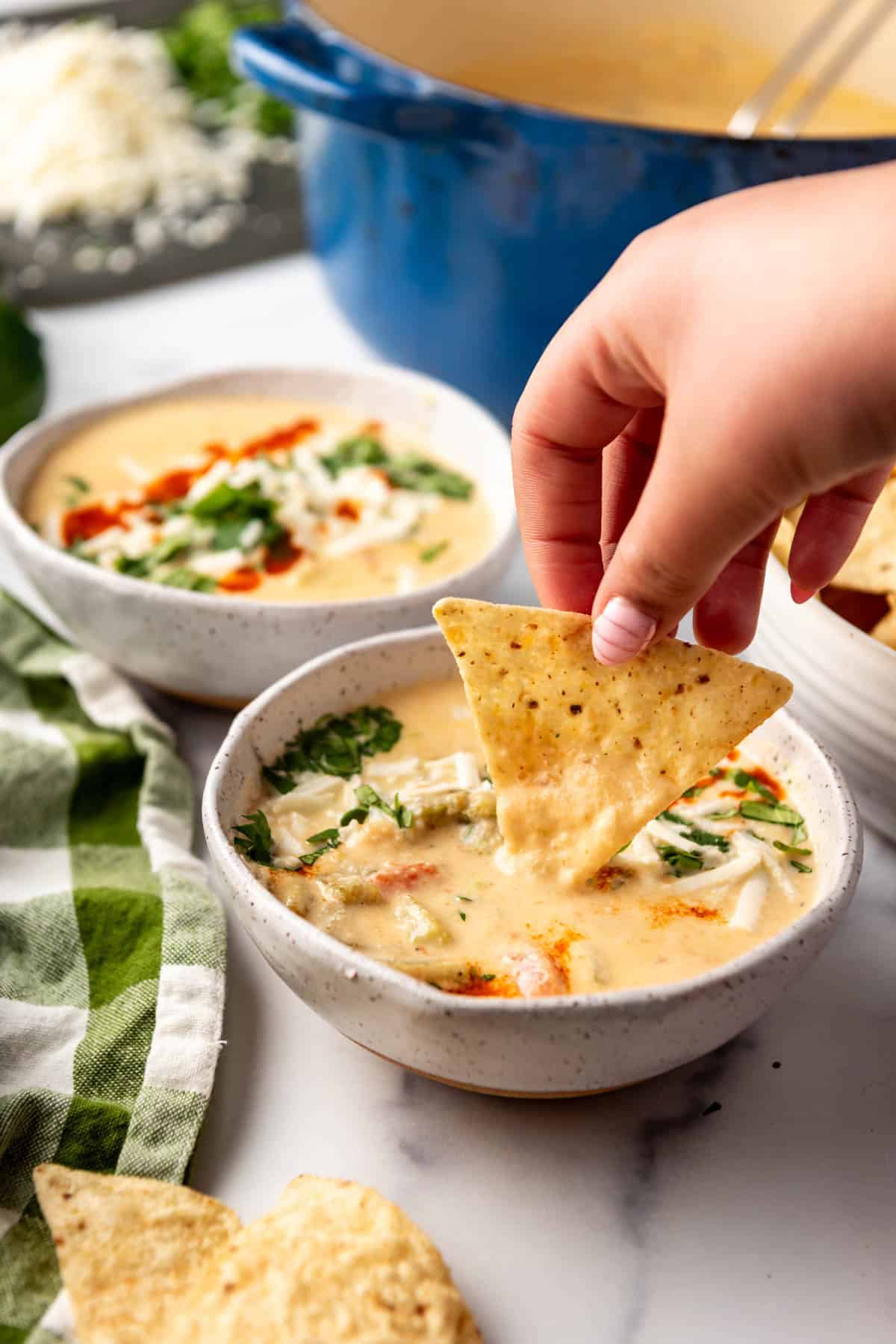 A hand dipping a tortilla chip into a bowl of queso.