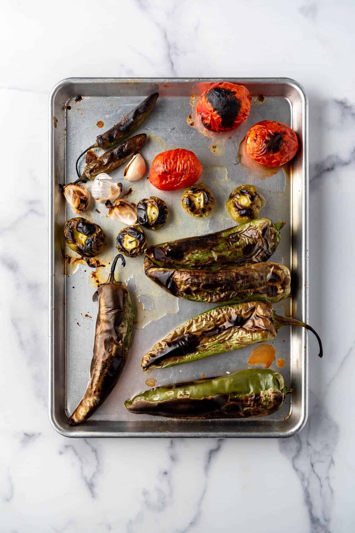 Roasted Anaheim peppers, tomatillos, tomatoes, and garlic on a baking sheet.