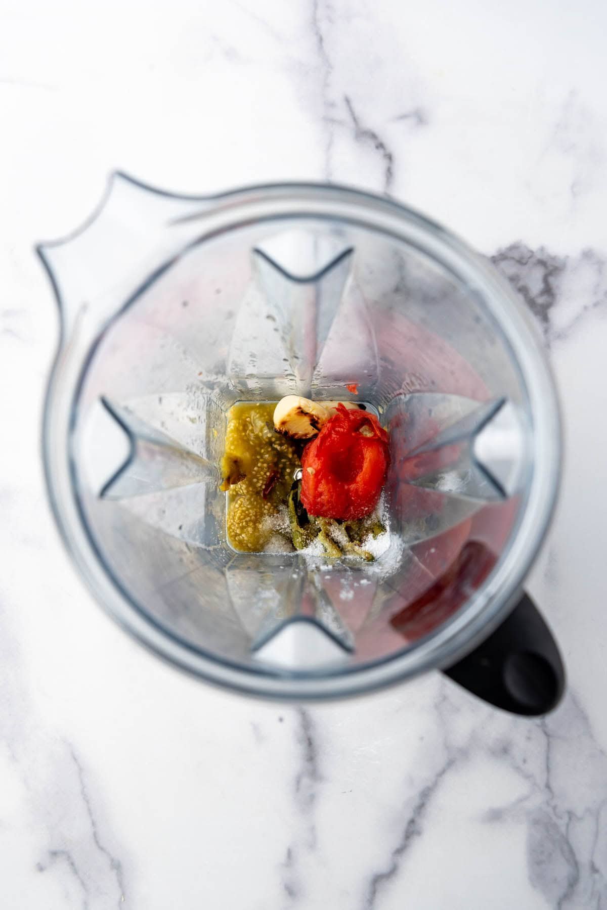 A blender with roasted tomato, garlic, and tomatillo in it.