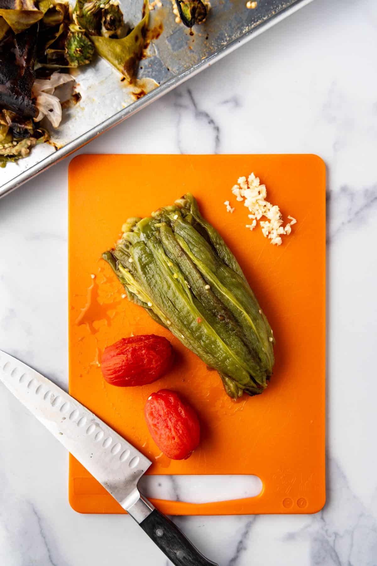 Roasted Anaheim peppers with stems and seeds removed on a cutting board with roasted tomatoes with skins removed and minced garlic.