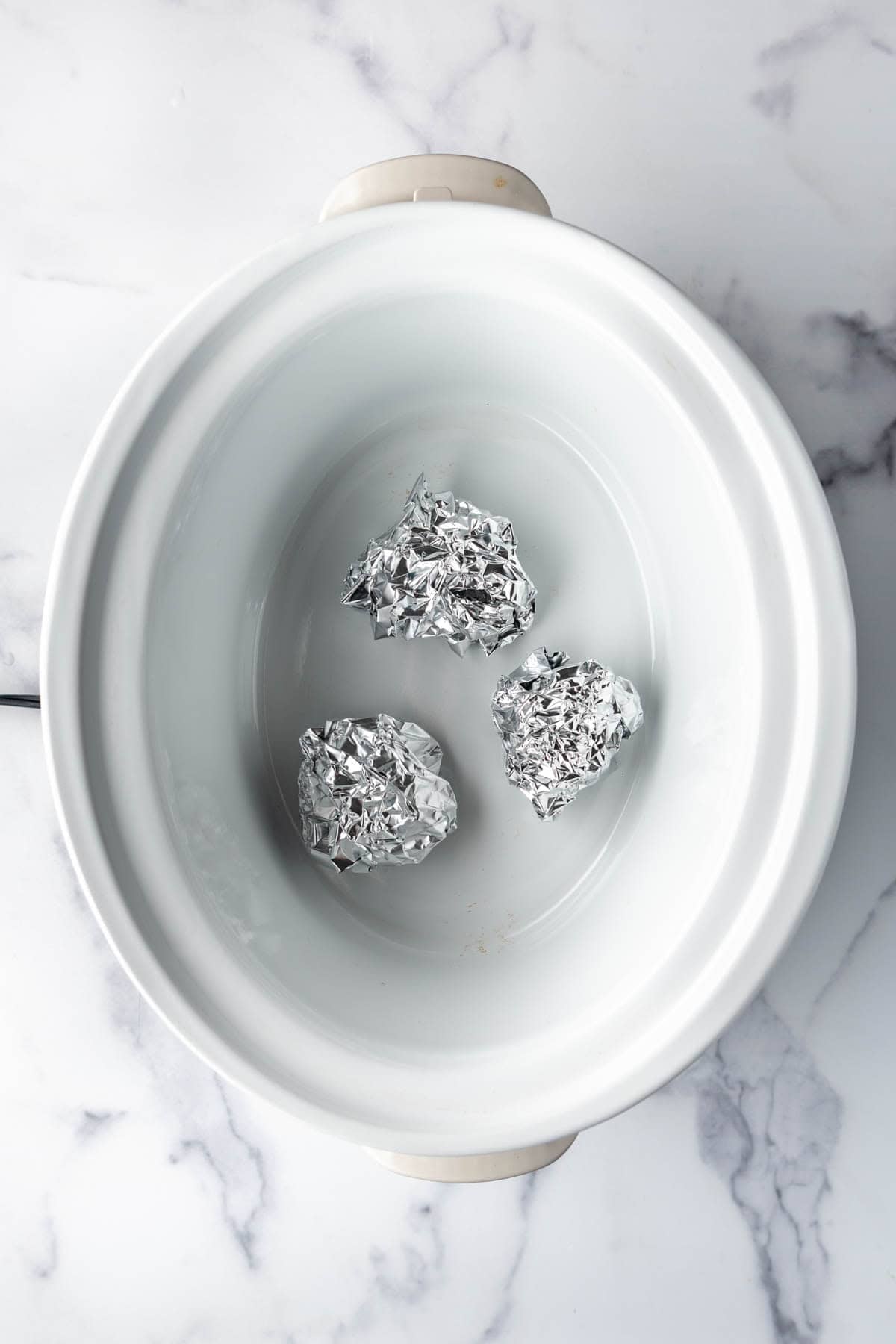 Balls of aluminum foil in a white slow cooker.