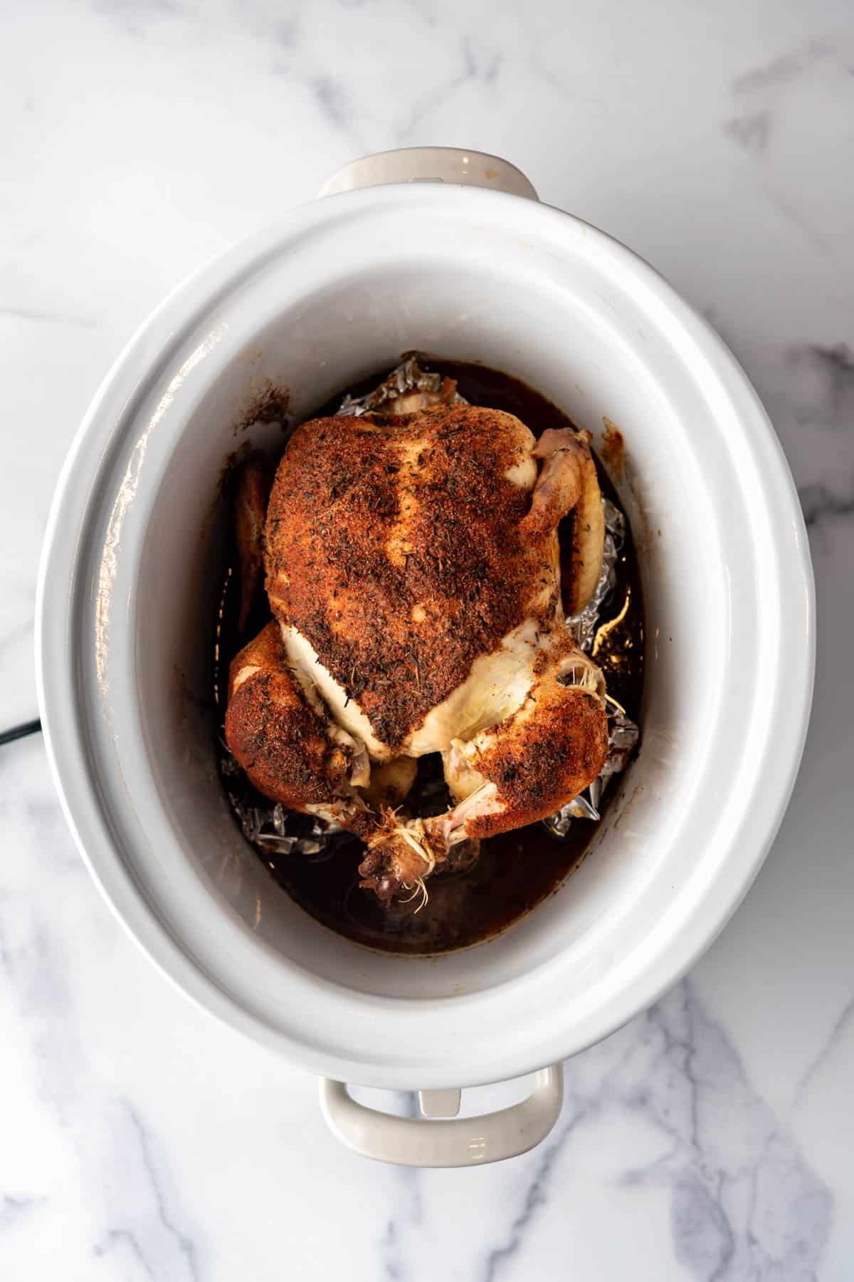 An overhead image of a whole chicken in a slow cooker.