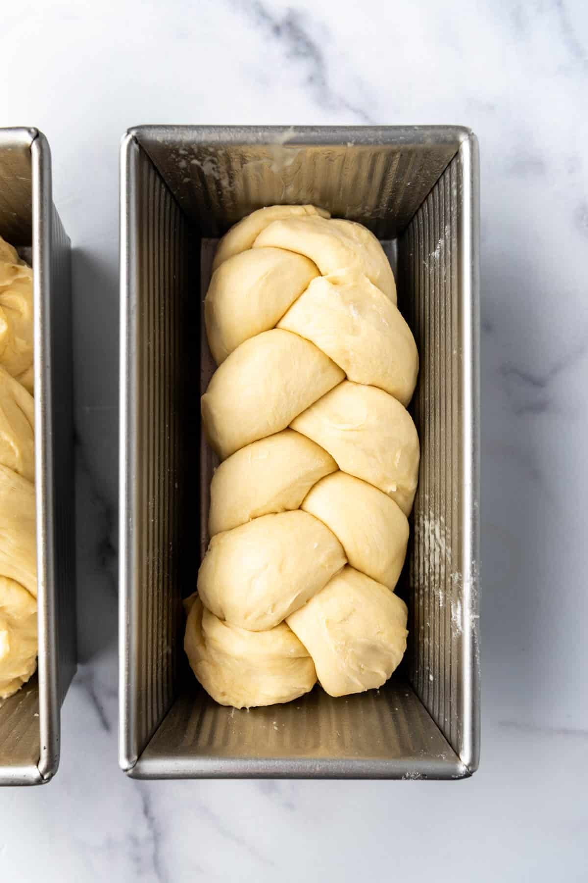 A three-strand braid of brioche bread dough in a loaf pan.