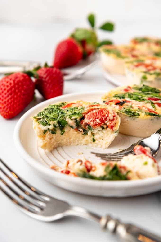 Egg white bites with a bite taken out of one of them on a plate with strawberries in the background.
