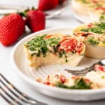 Egg white bites with a bite taken out of one of them on a plate with strawberries in the background.