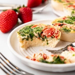 Egg white bites with a bite taken out of one of them on a plate with strawberries in the background.