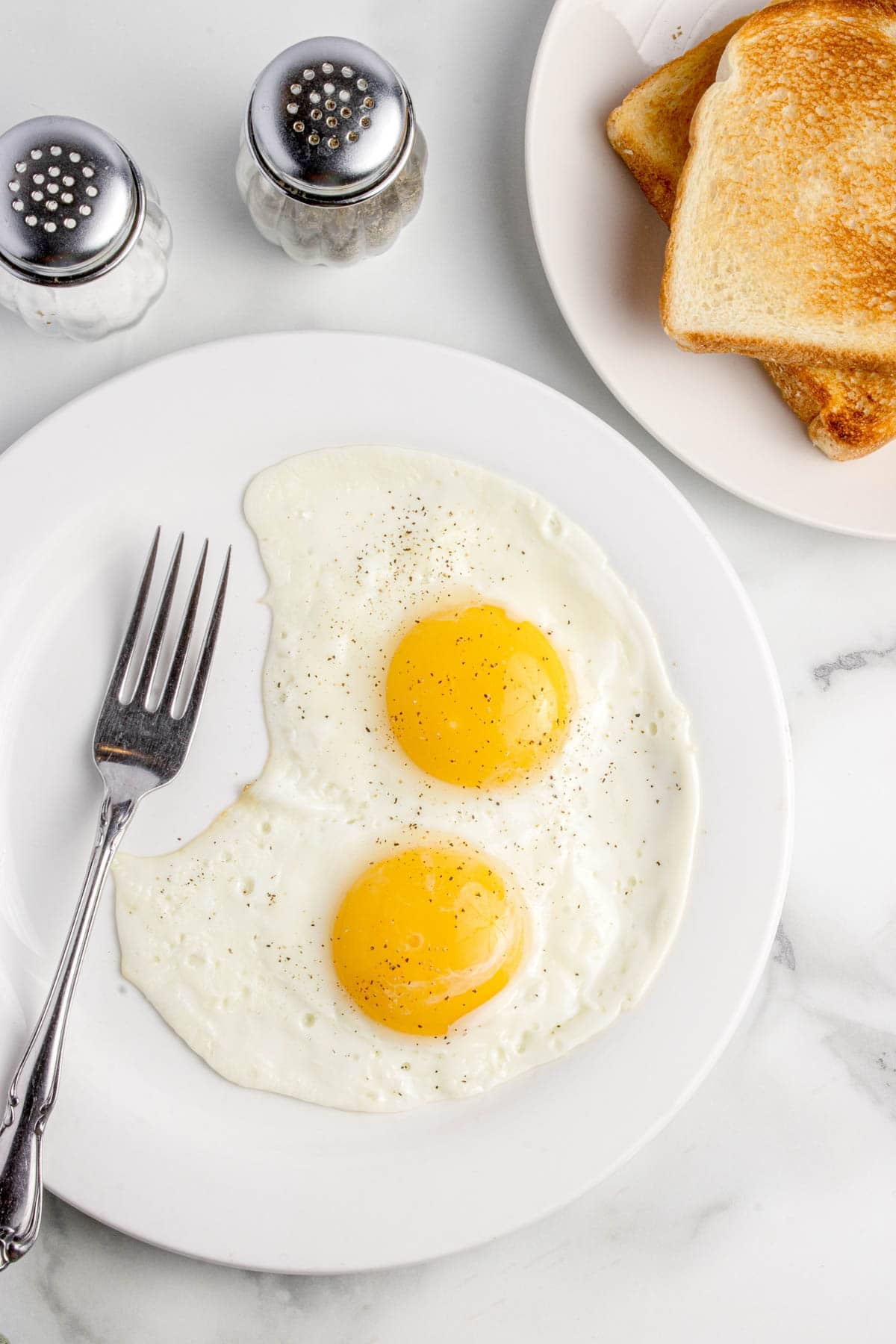 An overhead image of two sunny side up eggs on a plate with toast nearby.
