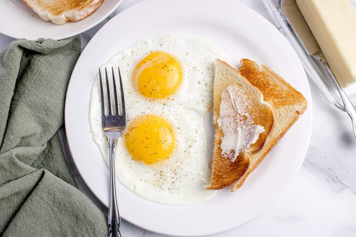 A plate with two sunny side up eggs and a toast with butter and a fork.