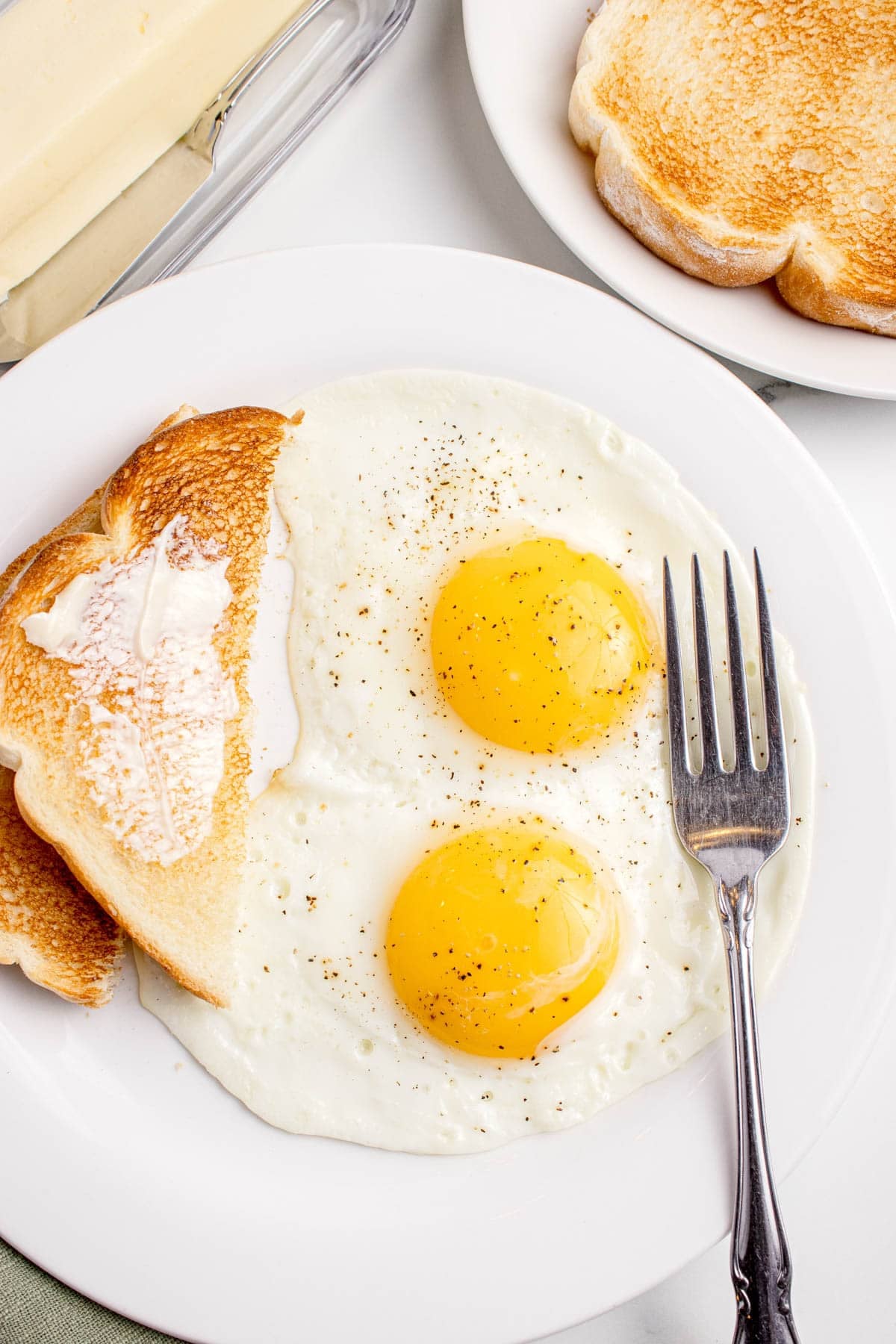 Tunny sunny side up eggs on a plate with buttered toast and a fork.