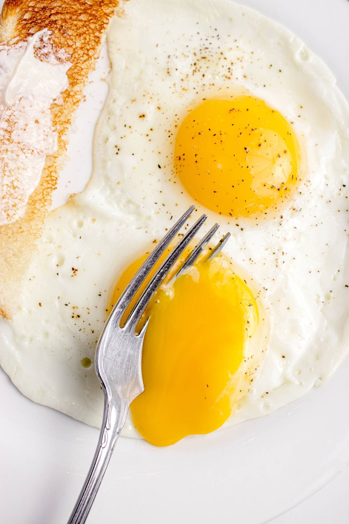 A close up image of a fork breaking soft set yolks in sunny side up eggs.