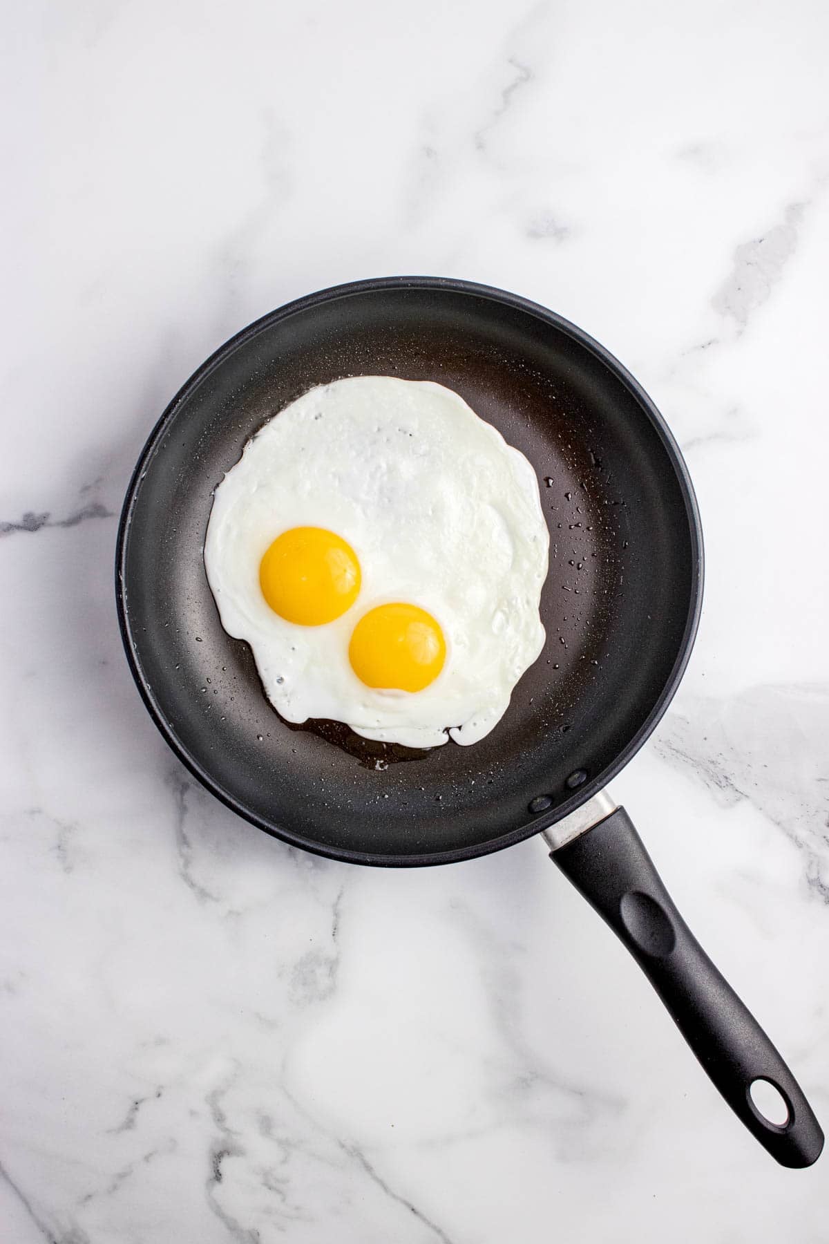 An image of two perfectly cooked sunny side up eggs in a nonstick pan.