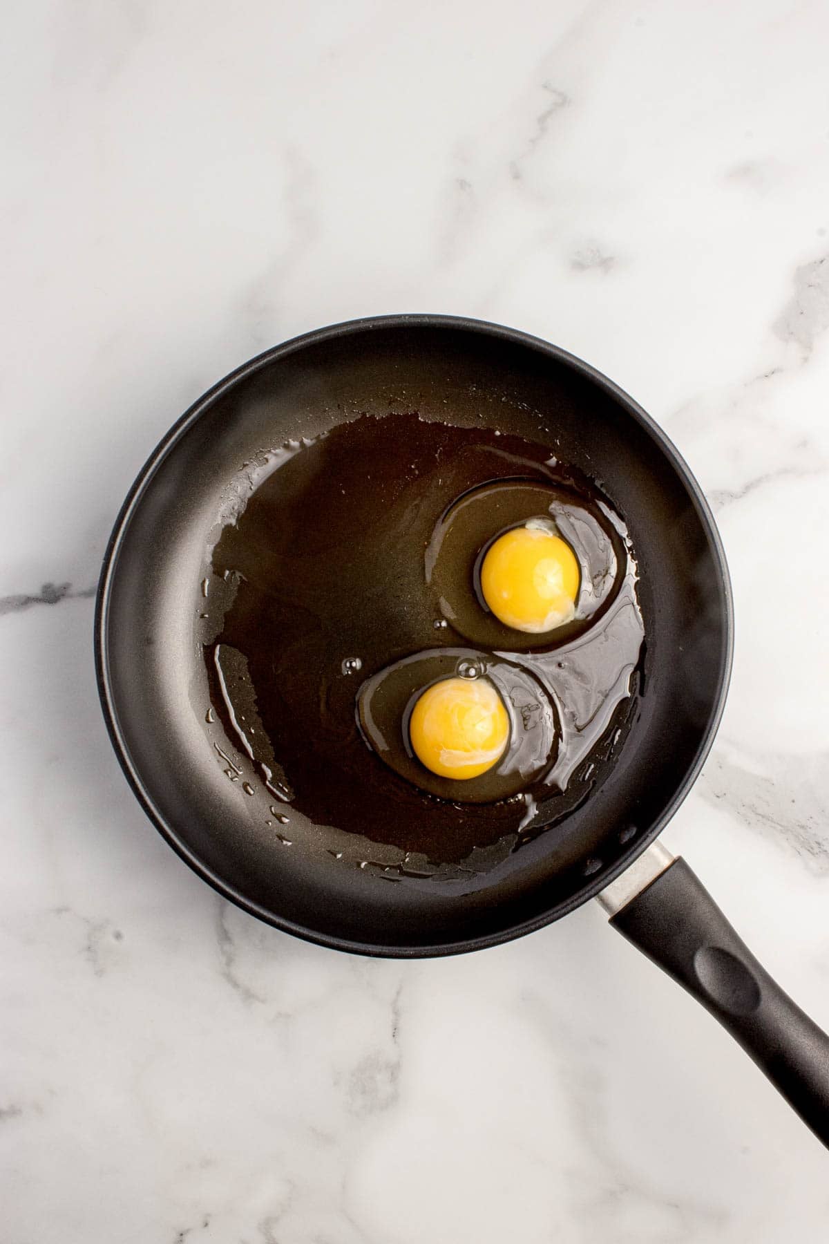 Adding two eggs to a nonstick pan with a little oil in it.