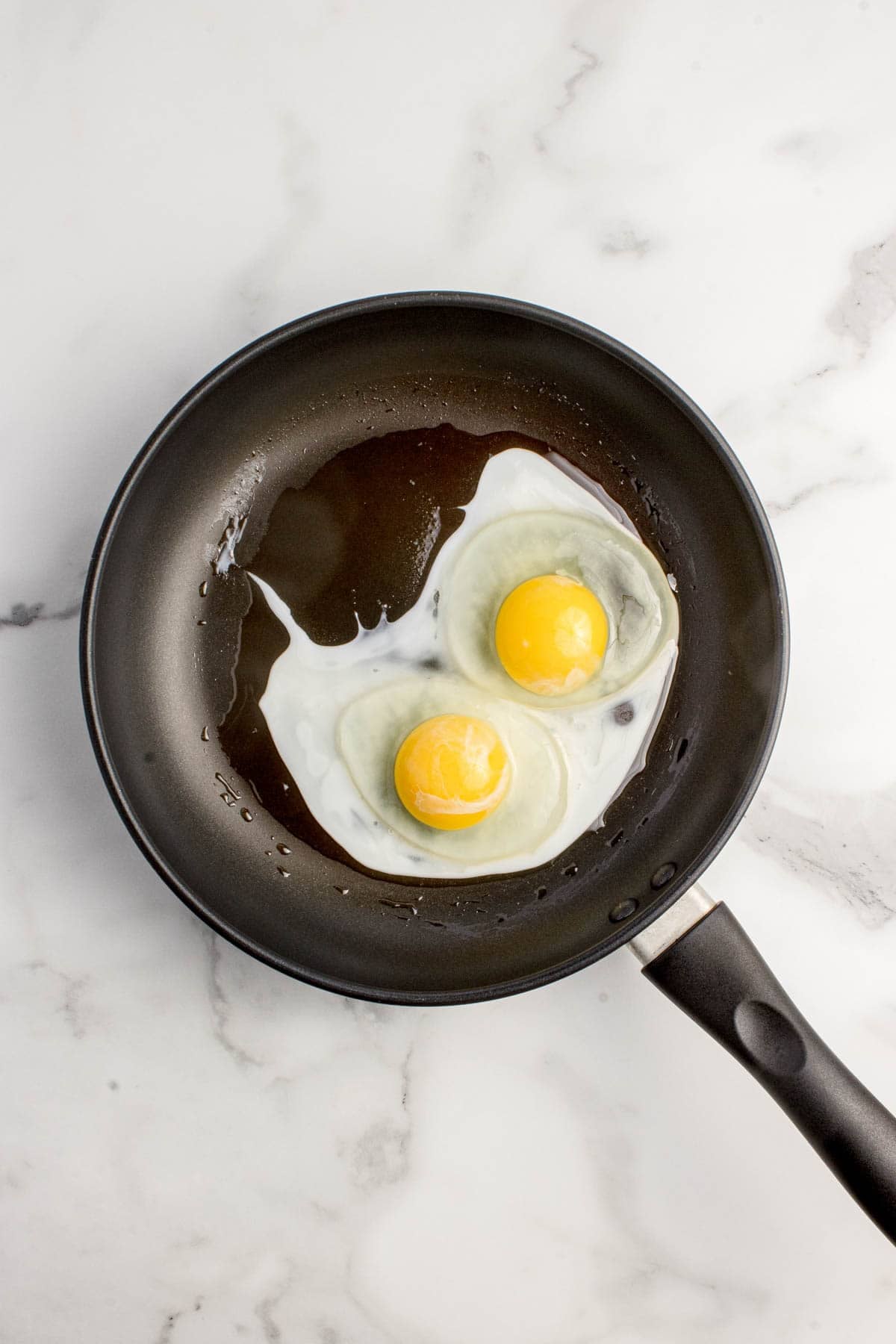 Two partially cooked eggs in a nonstick pan.