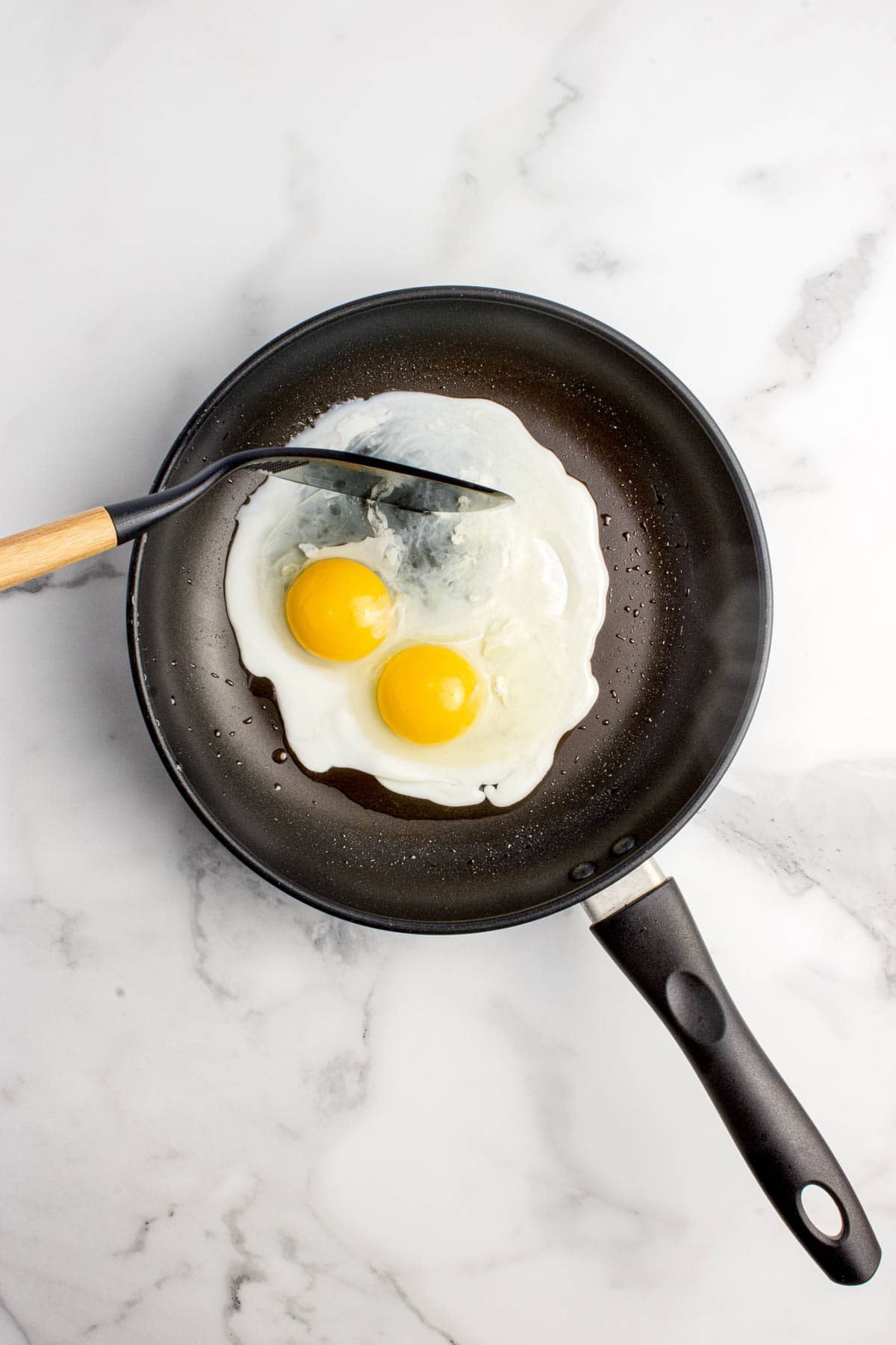 Two partially fried eggs in a pan.