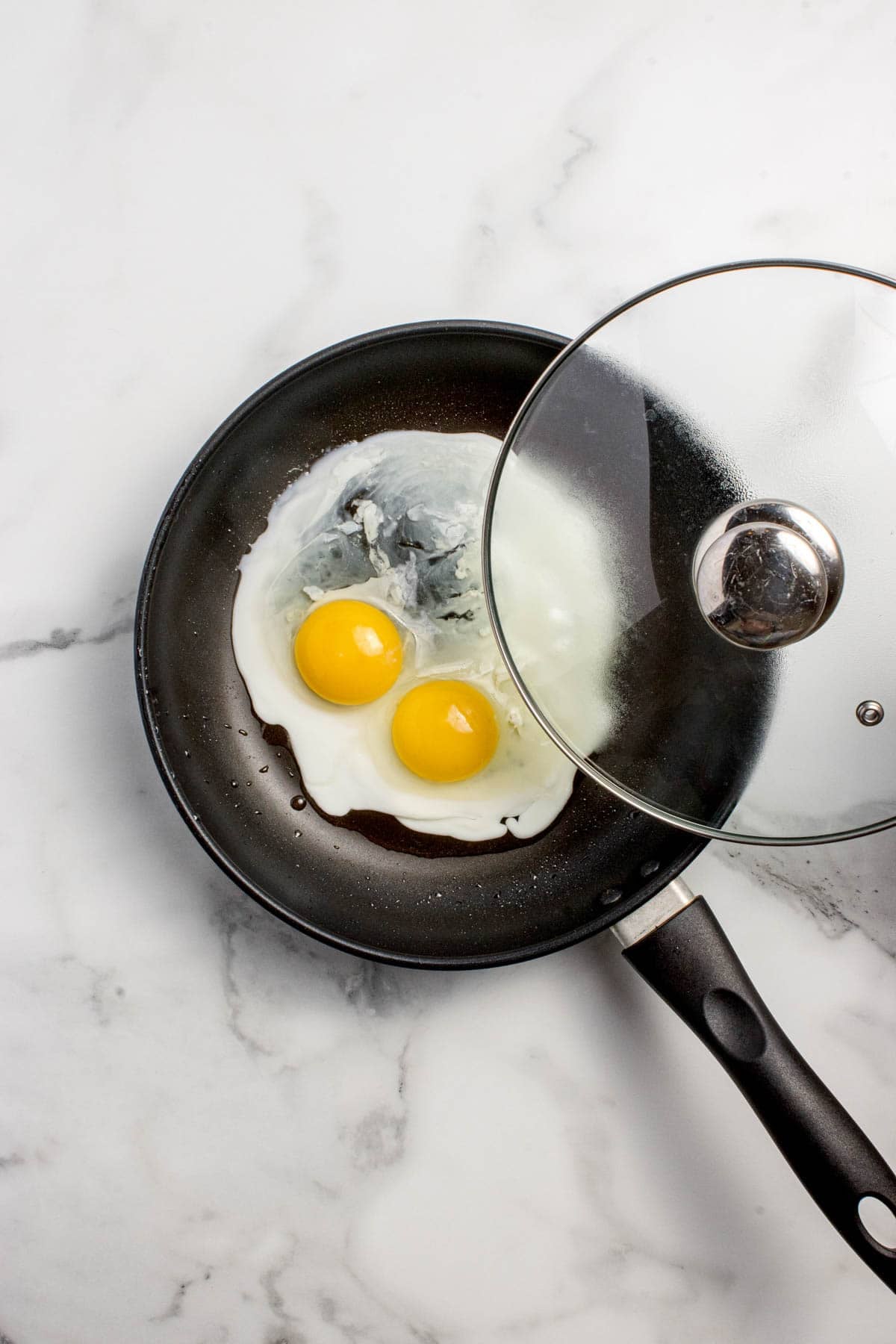 Covering two partially fried eggs with a glass lid.