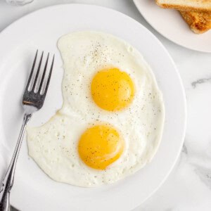 An overhead image of two sunny side up eggs on a plate with toast nearby.