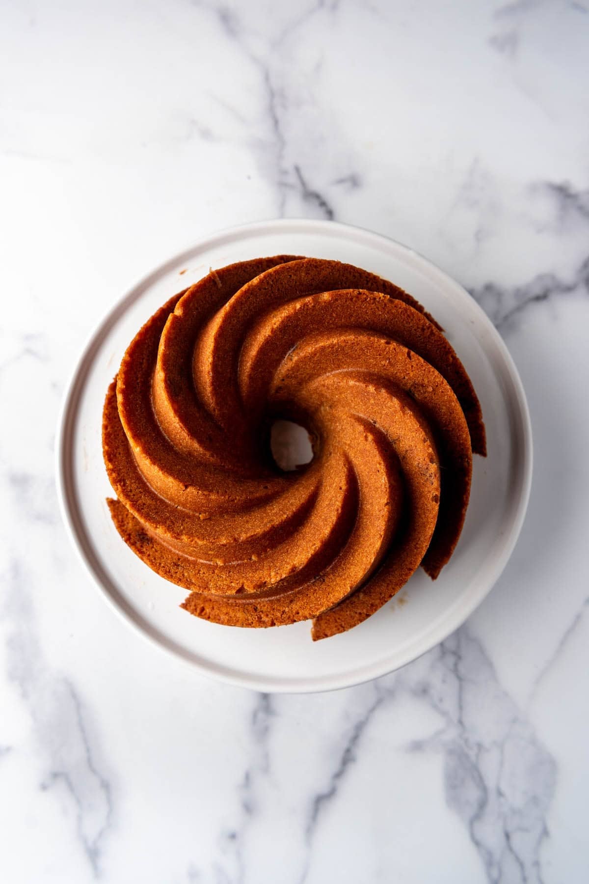 A bundt cake on a white cake stand before being decorated with a glaze.