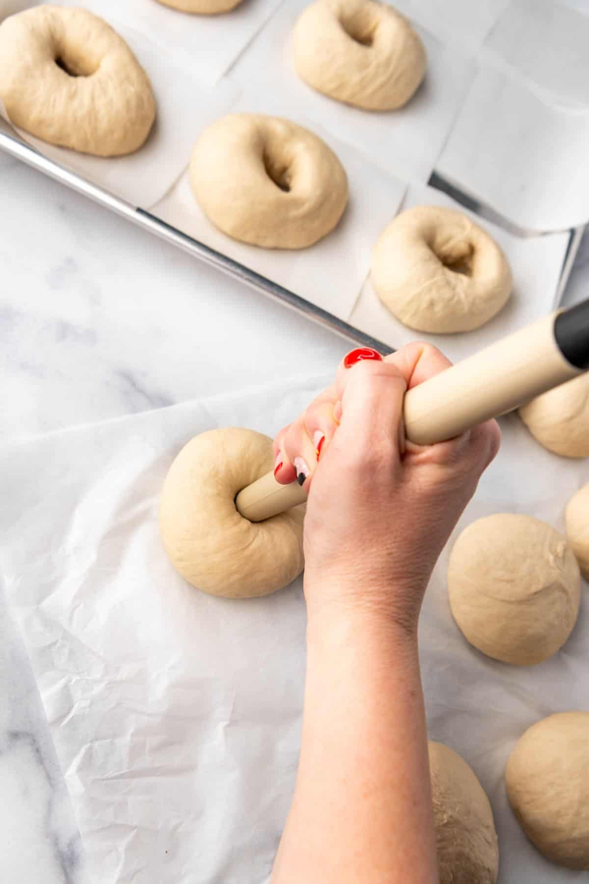 Using a bread dough tool to poke holes in the center of balls of dough to make bagels.