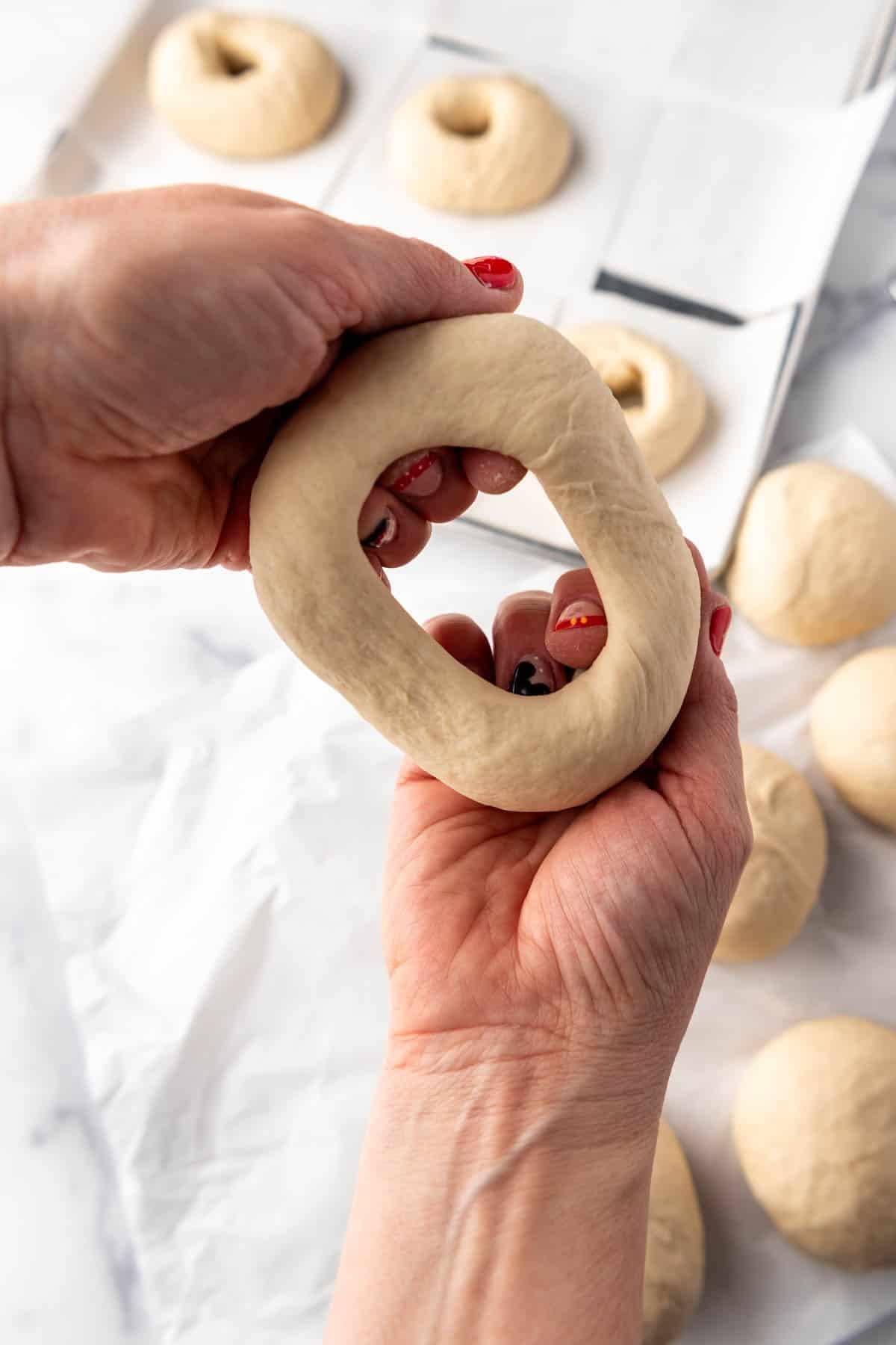 Hands showing dough being stretched out into a bagel shape.
