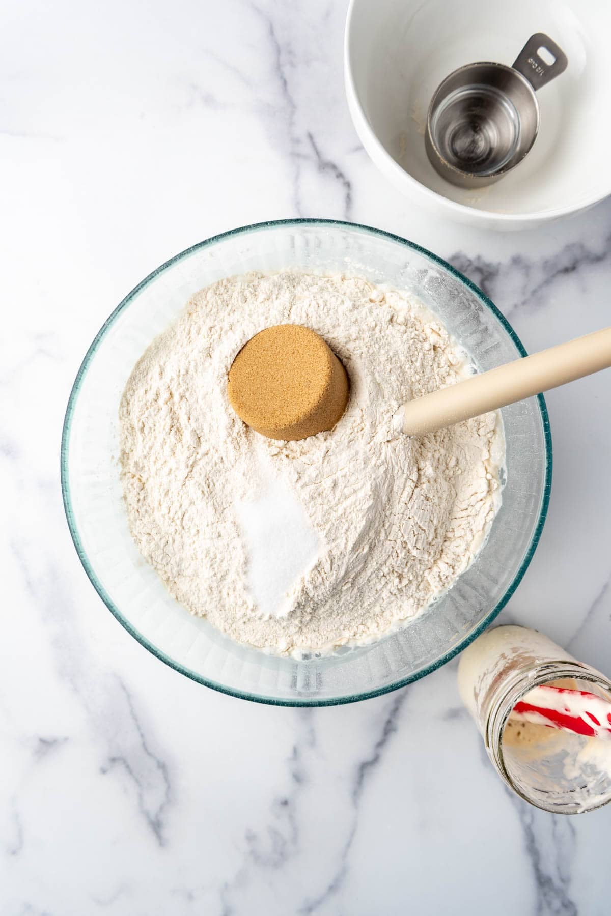 Adding flour, brown sugar, and salt to sourdough starter and water in a large mixing bowl.