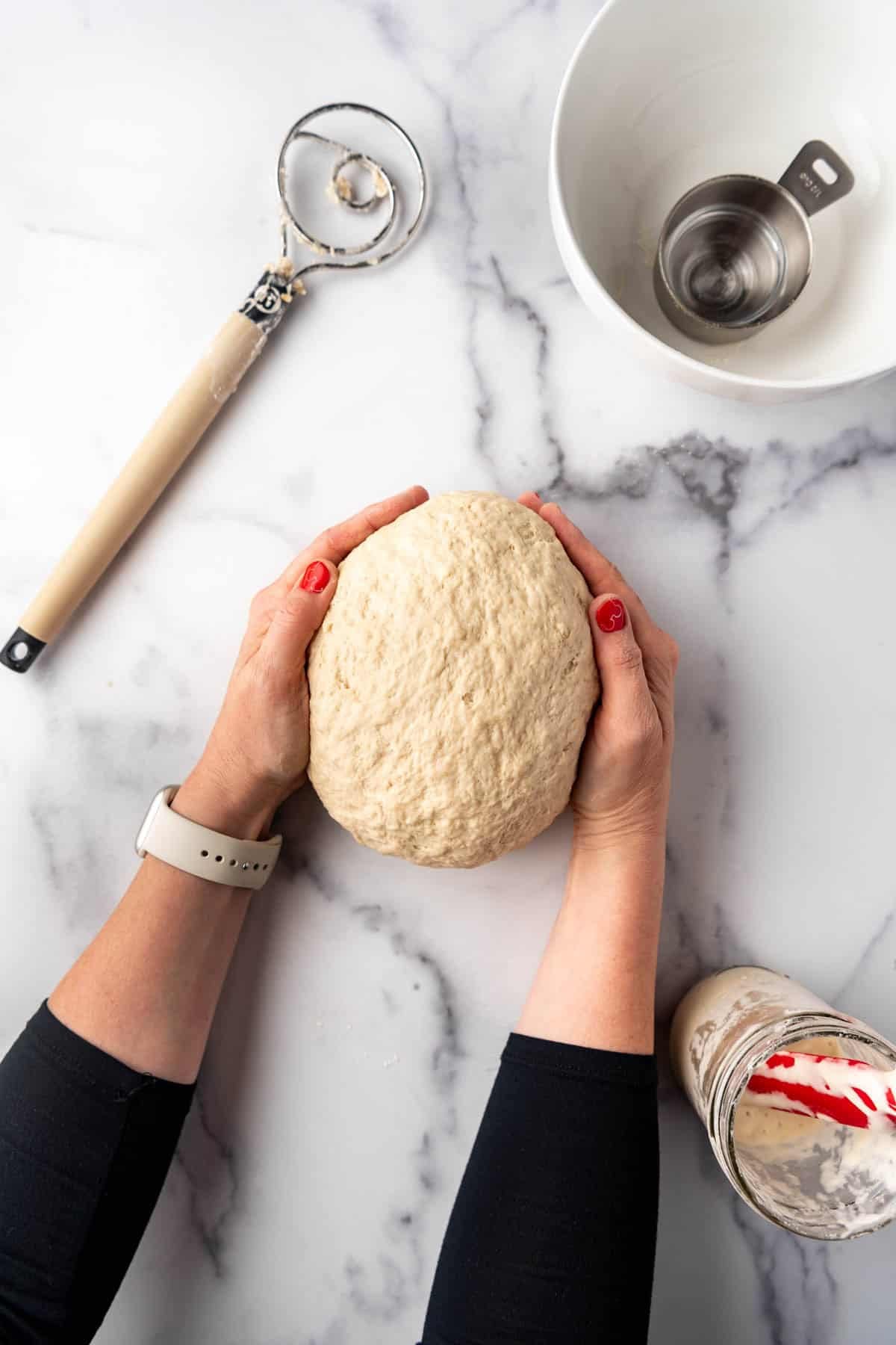 A ball of sourdough bagel dough with hands holding it.