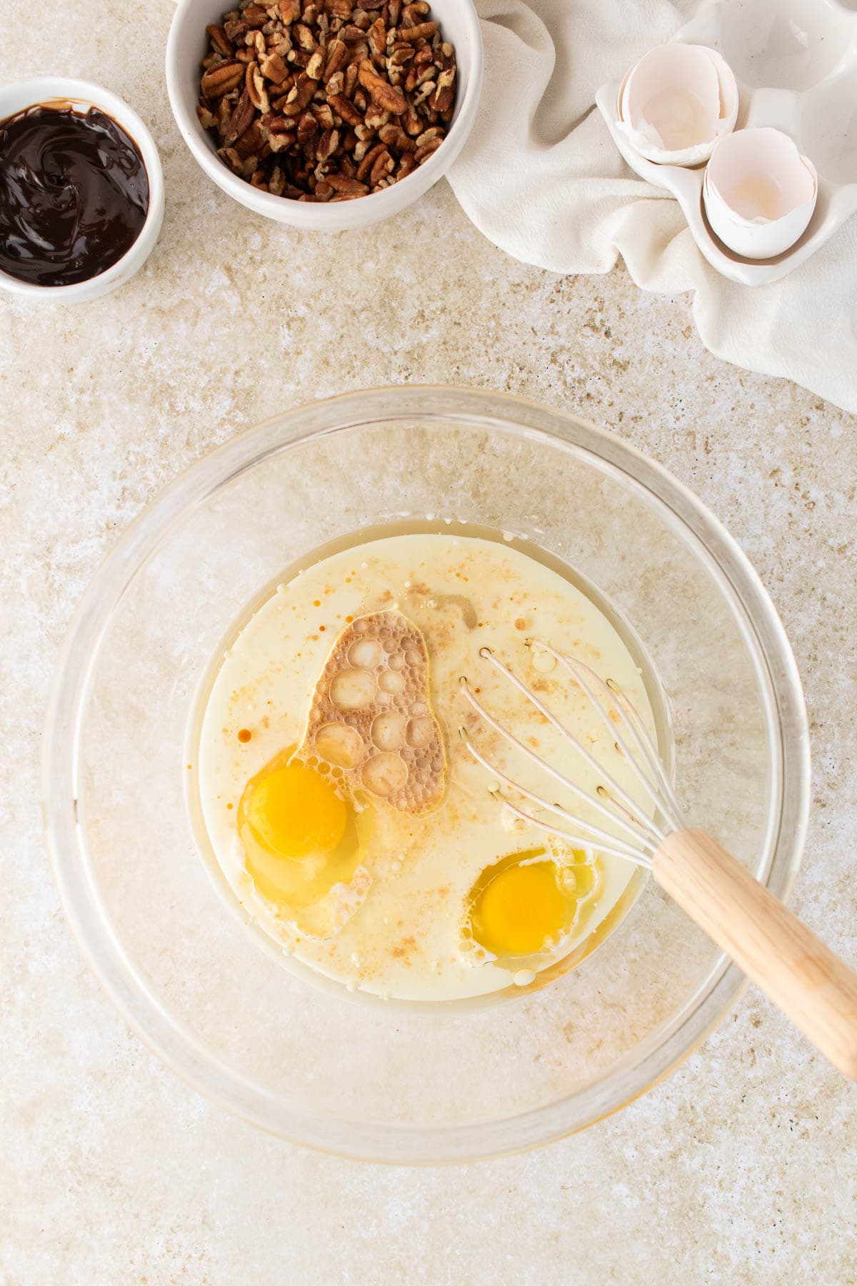 Whisking eggs, oil, milk, and vanilla in a glass mixing bowl.