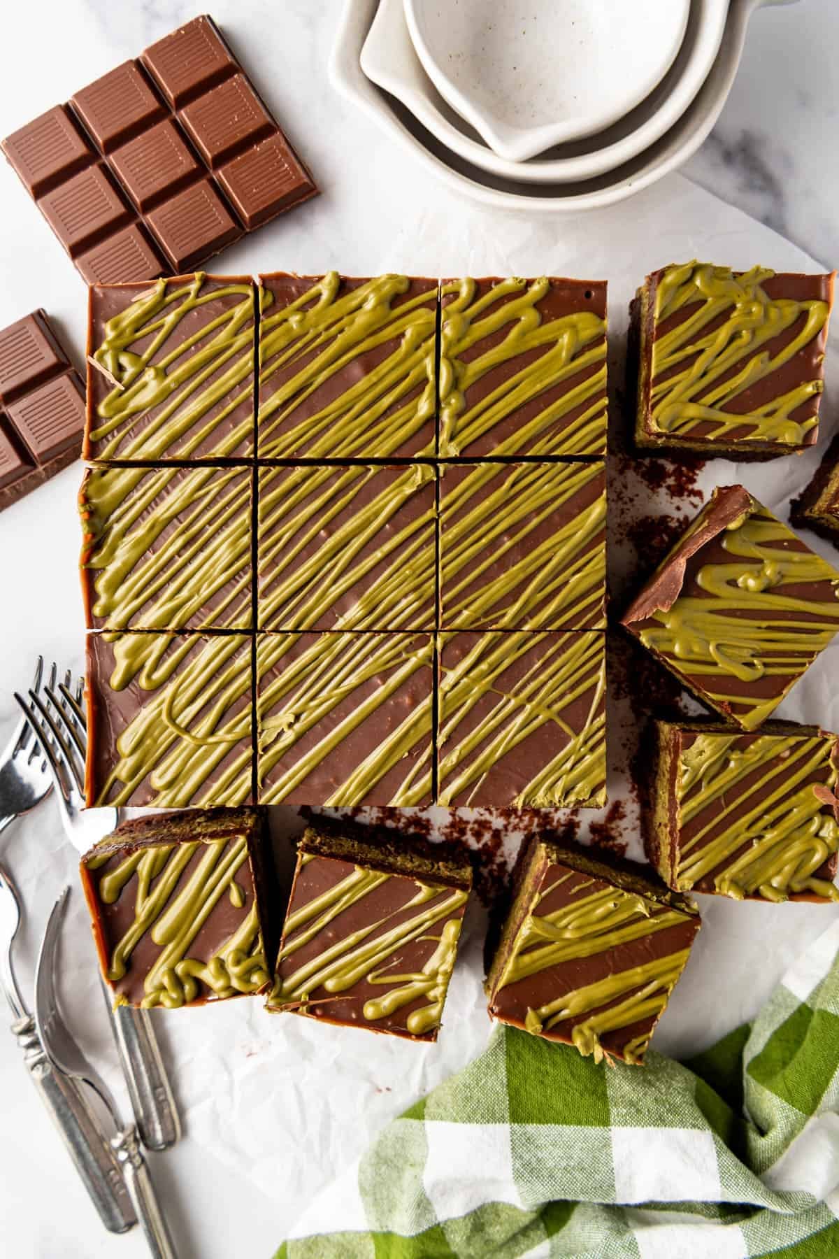 Homemade Dubai chocolate brownies next to chocolate bars and a green checkered linen.