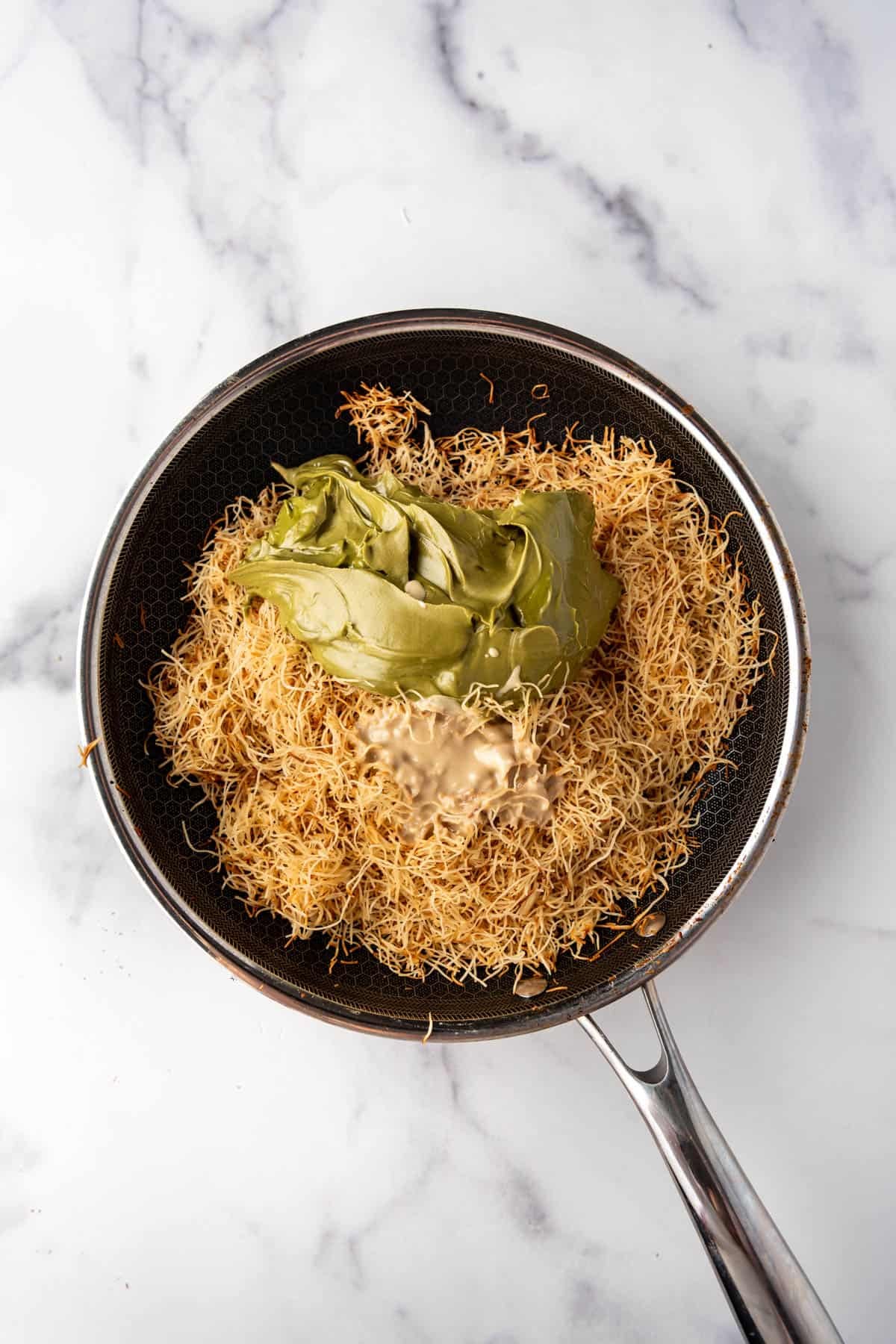Adding pistachio cream and tahini to toasted kataifi in a skillet.