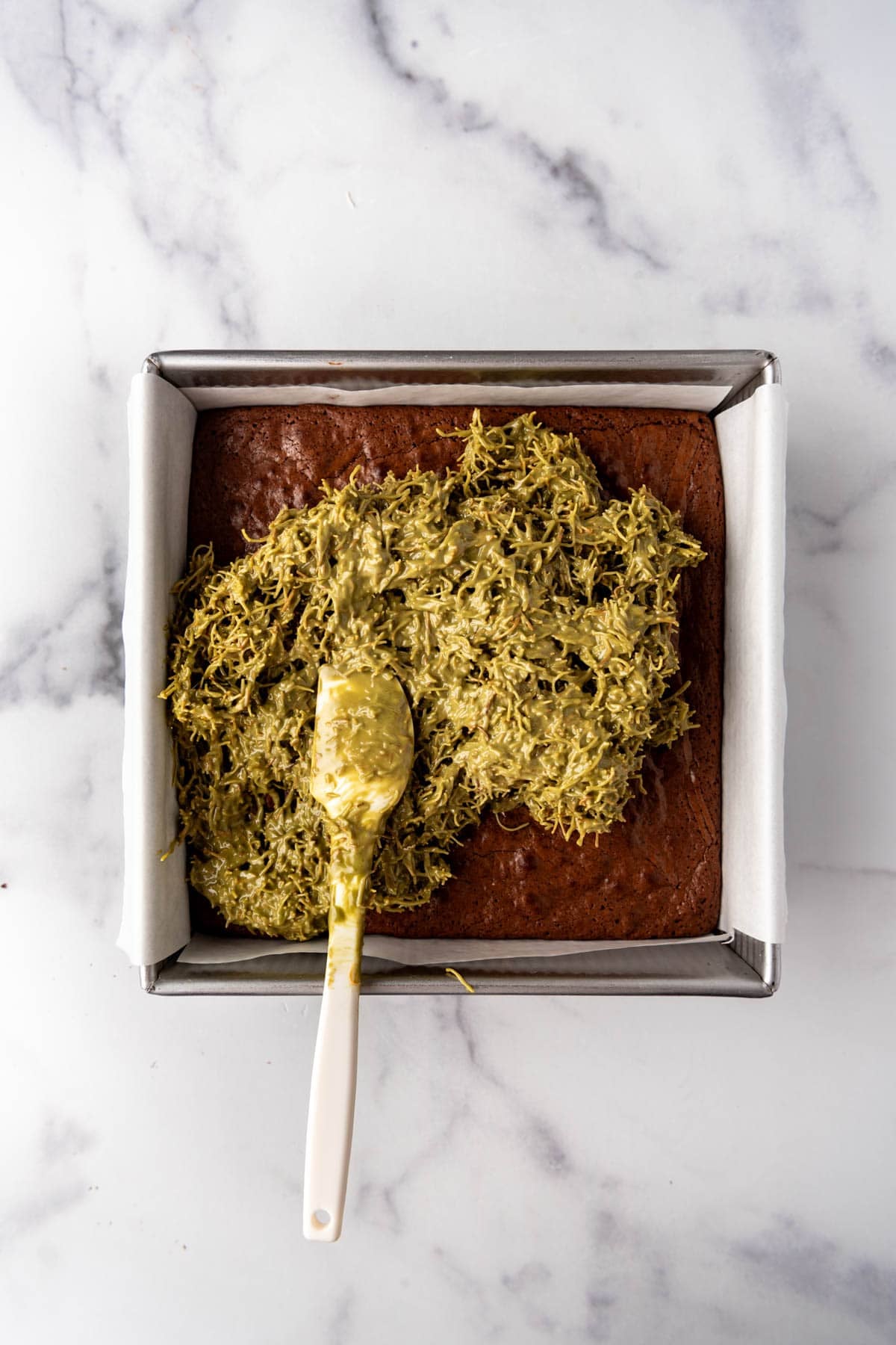 Spreading pistachio kataifi filling for Dubai brownies over a pan of fudgy brownies.