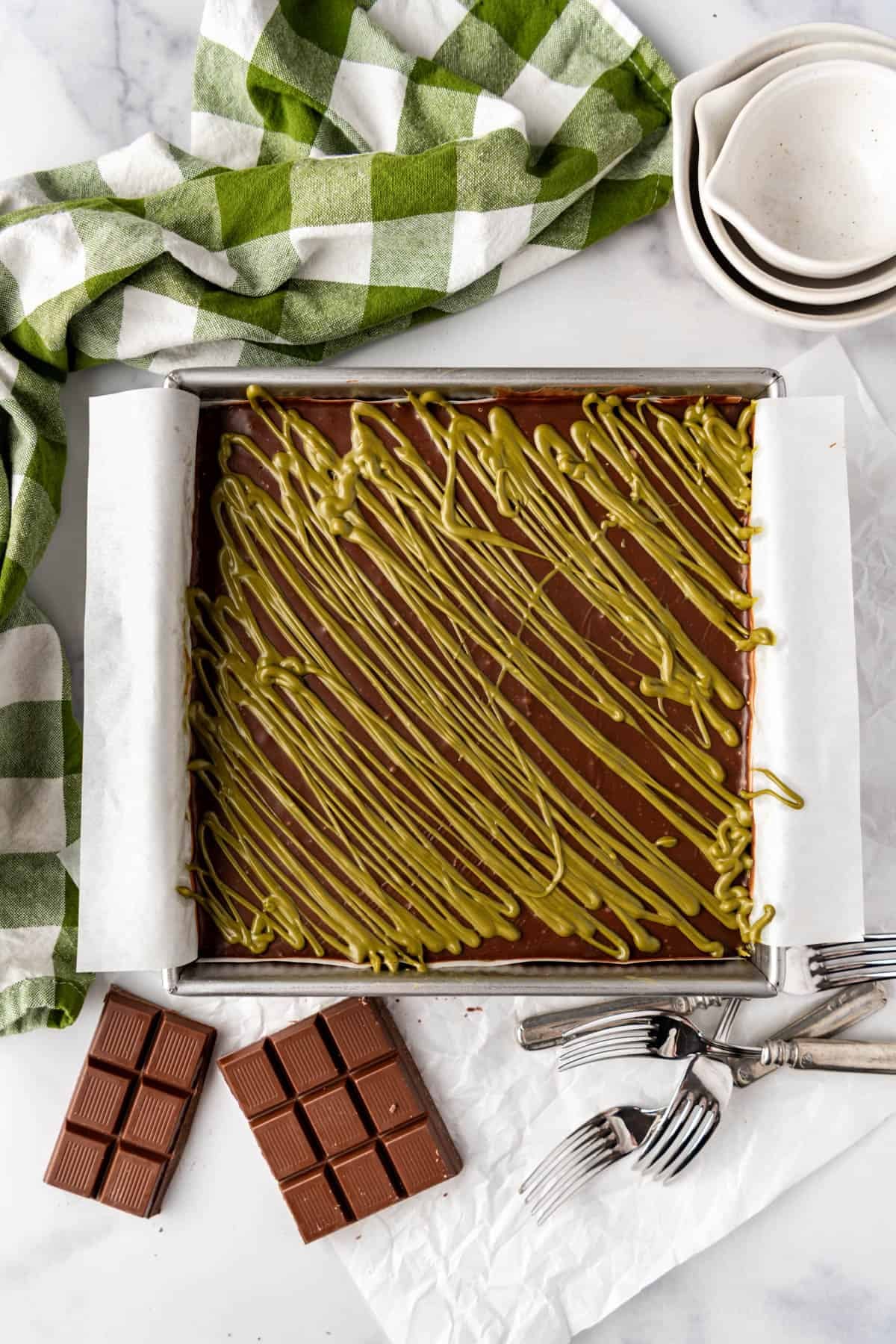 A pan of Dubai brownies with pistachio cream drizzled on top.