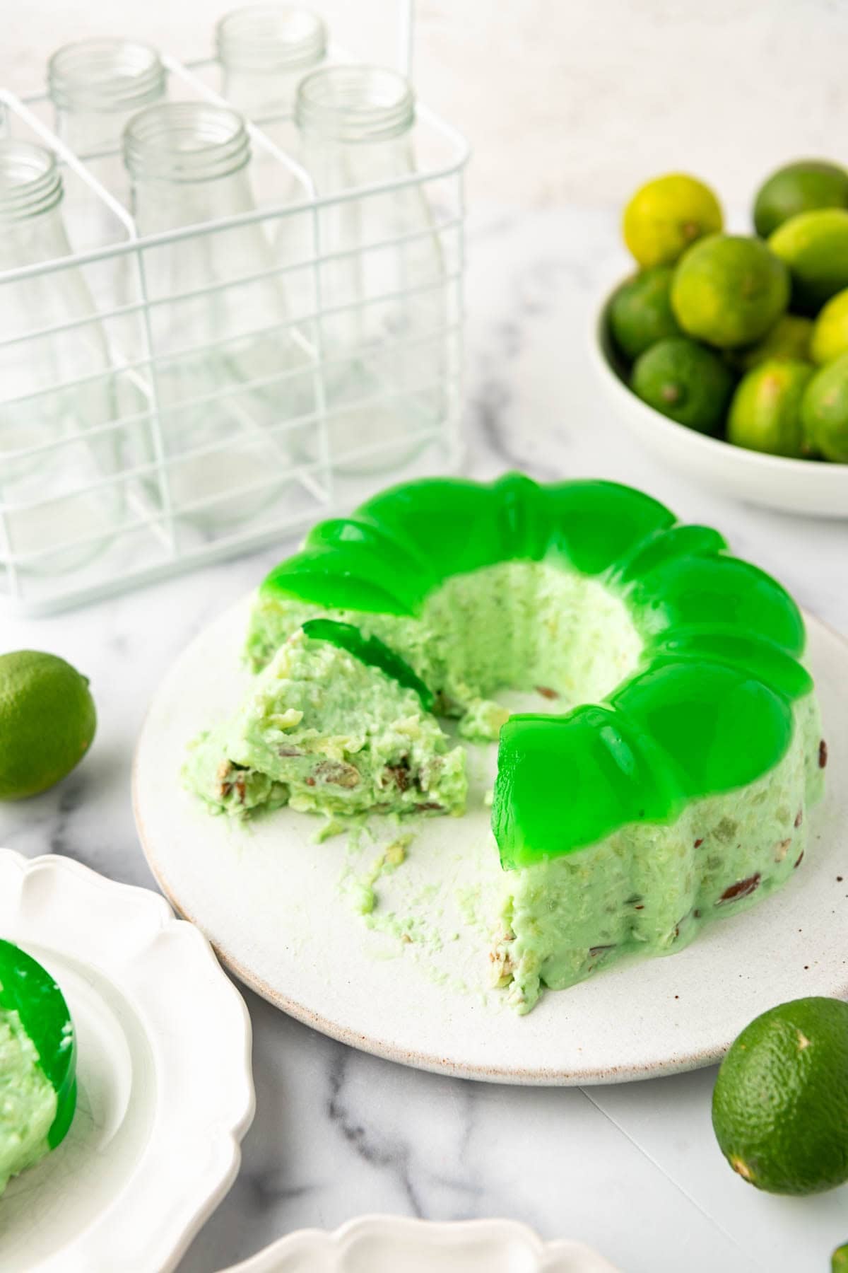 A partially sliced lime green jello mold with fresh limes nearby.