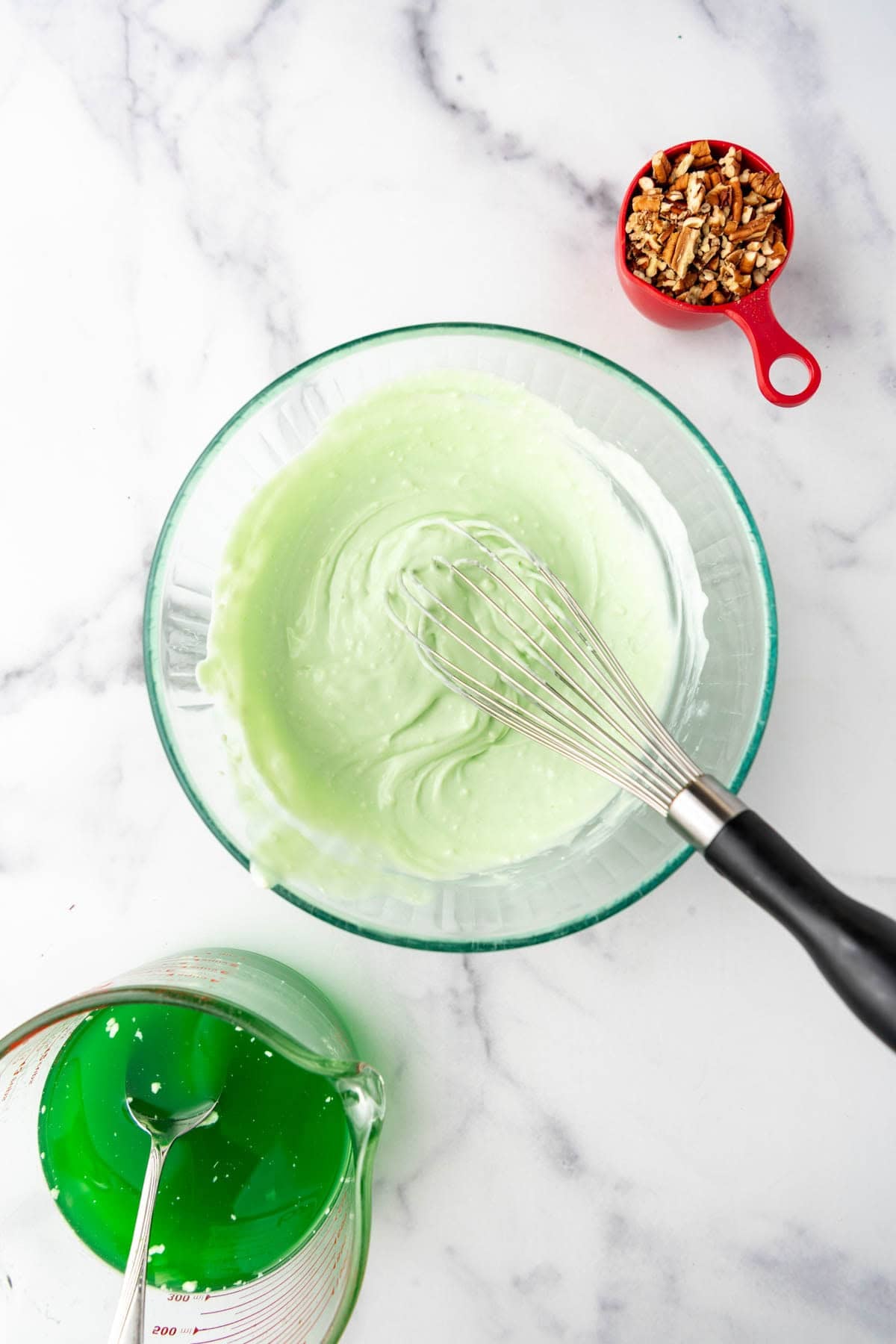 Whisking softened cream cheese into lime gelatin in a glass mixing bowl.