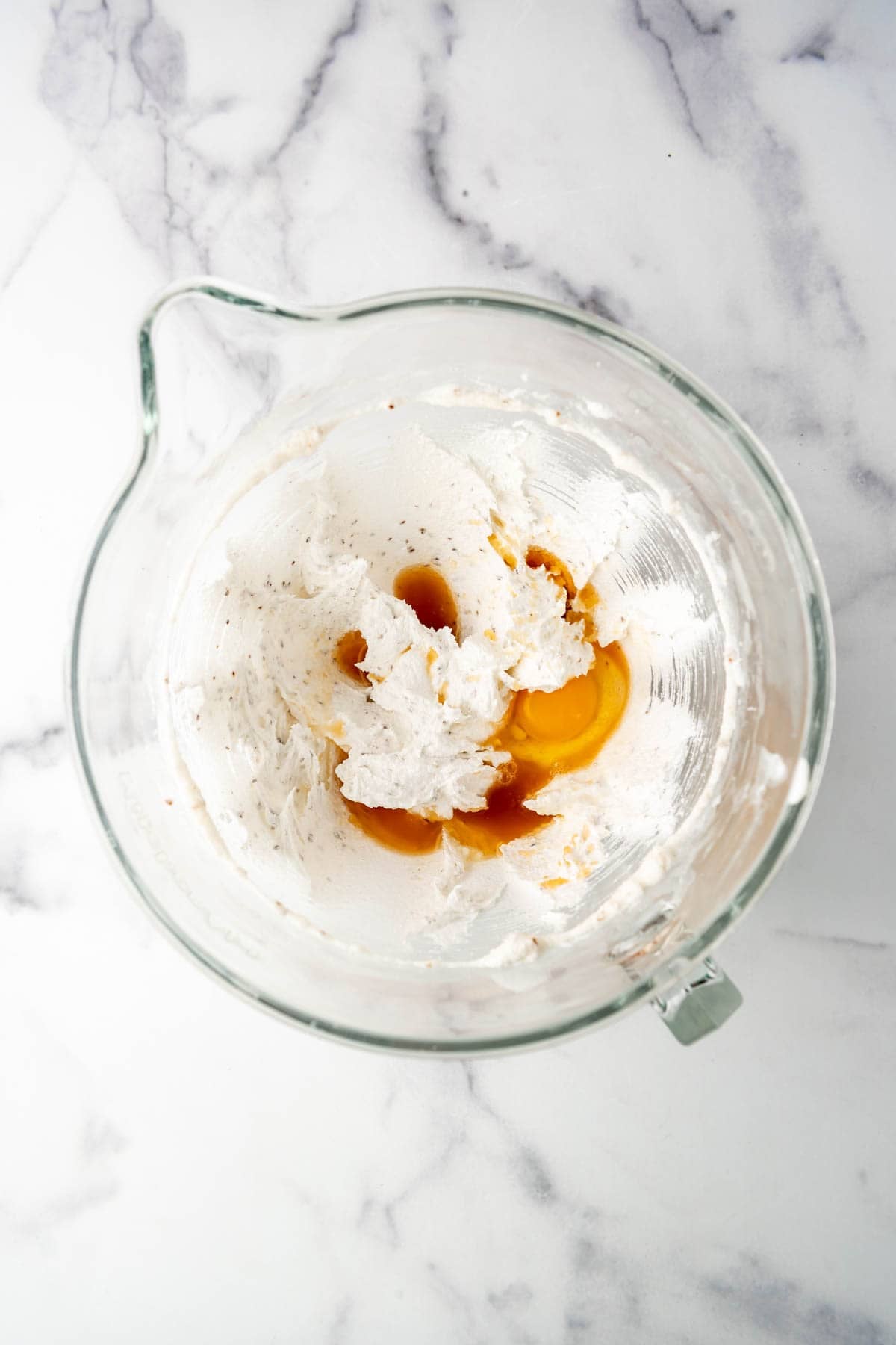 Adding eggs and vanilla to creamed shortening, sugar, and crushed anise seeds.
