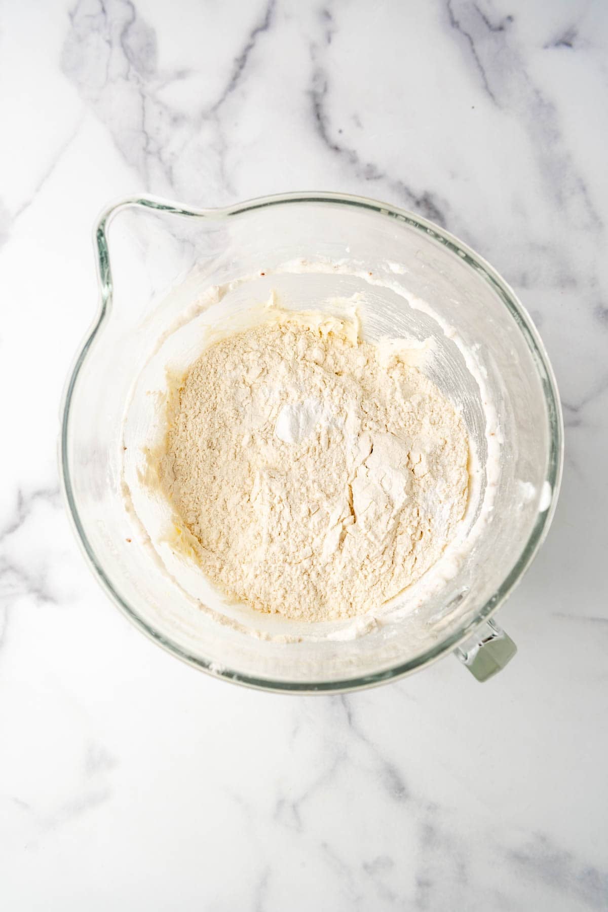 Adding dry ingredients to a mixing bowl to make a batch of biscochitos cookies.