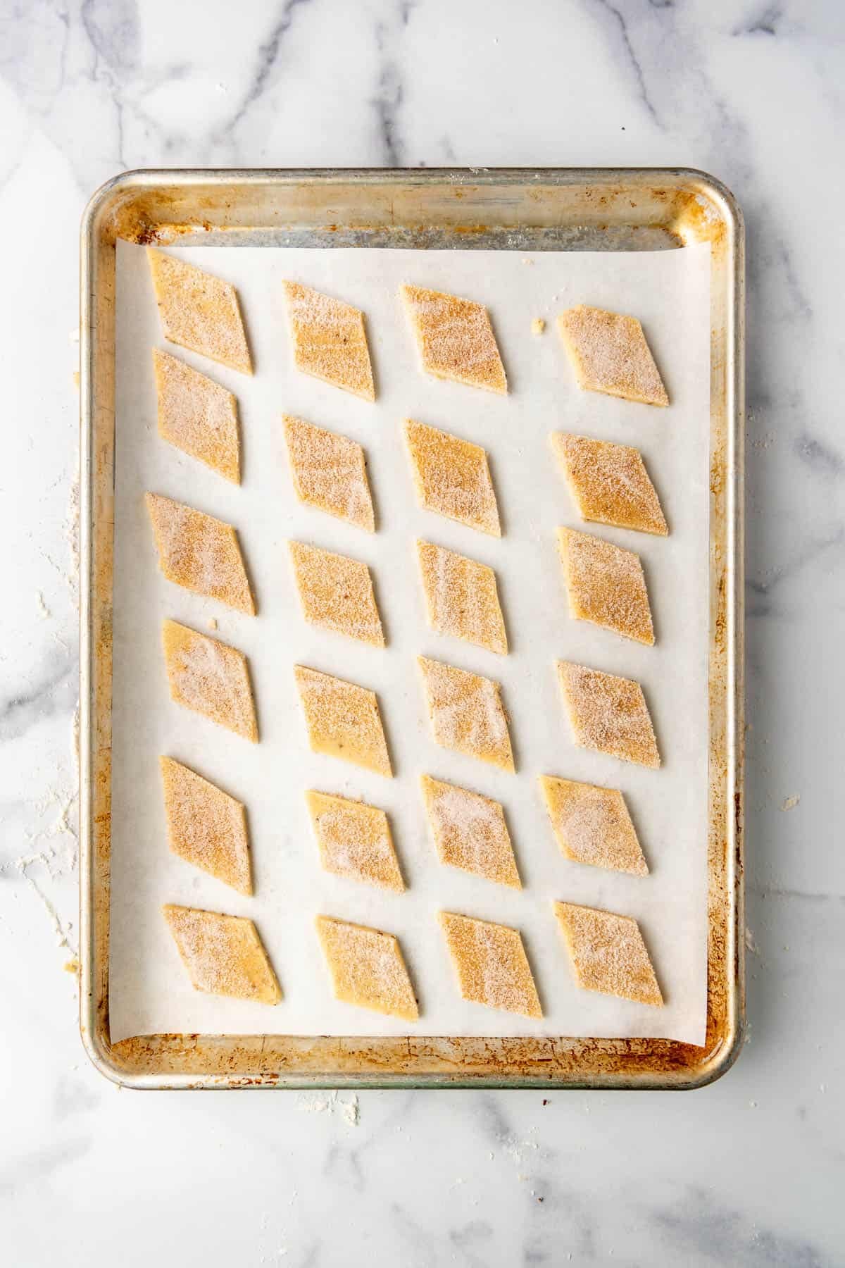 A baking sheet with diamond-shaped biscochito cookie dough on it. 