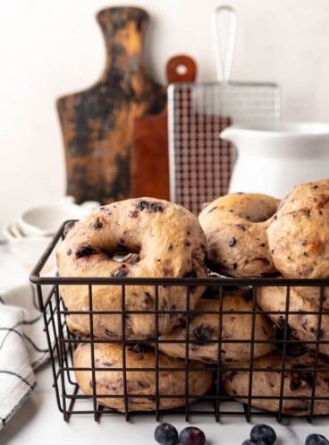 An image of homemade blueberry sourdough bagels in a black wire basket.