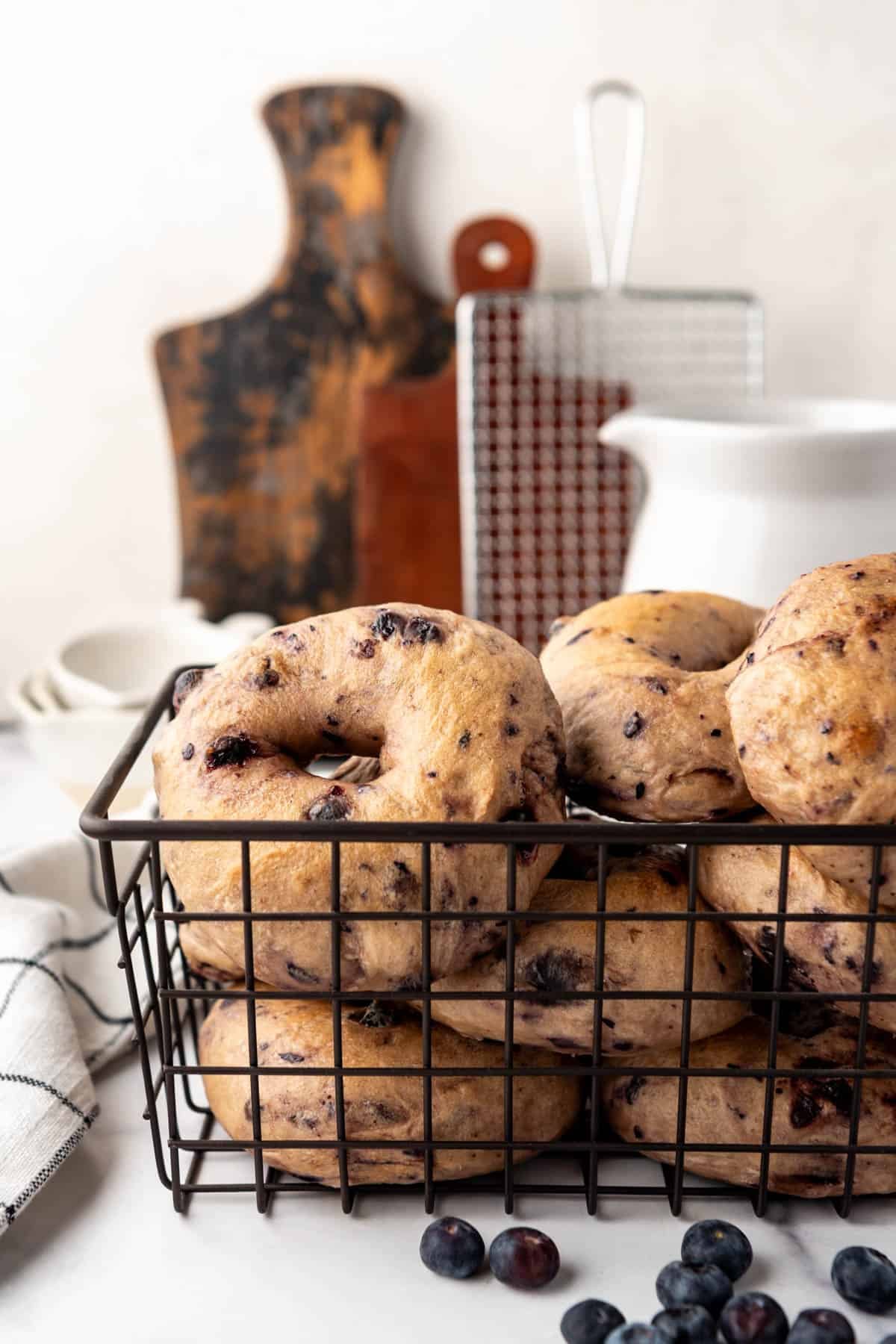 An image of homemade blueberry sourdough bagels in a black wire basket.