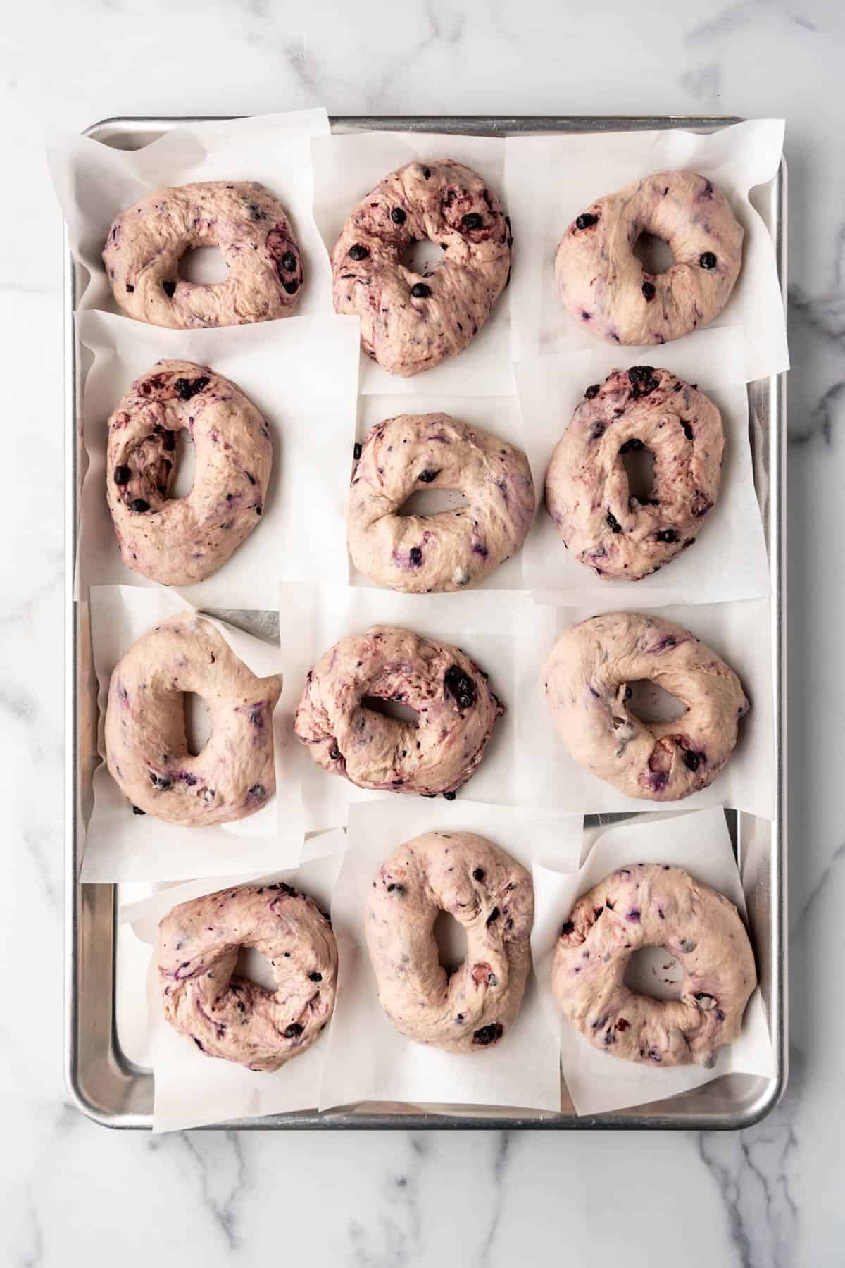 Shaped blueberry bagels on a large baking sheet.