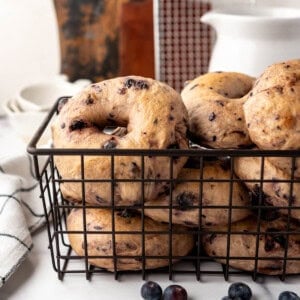 An image of homemade blueberry sourdough bagels in a black wire basket.