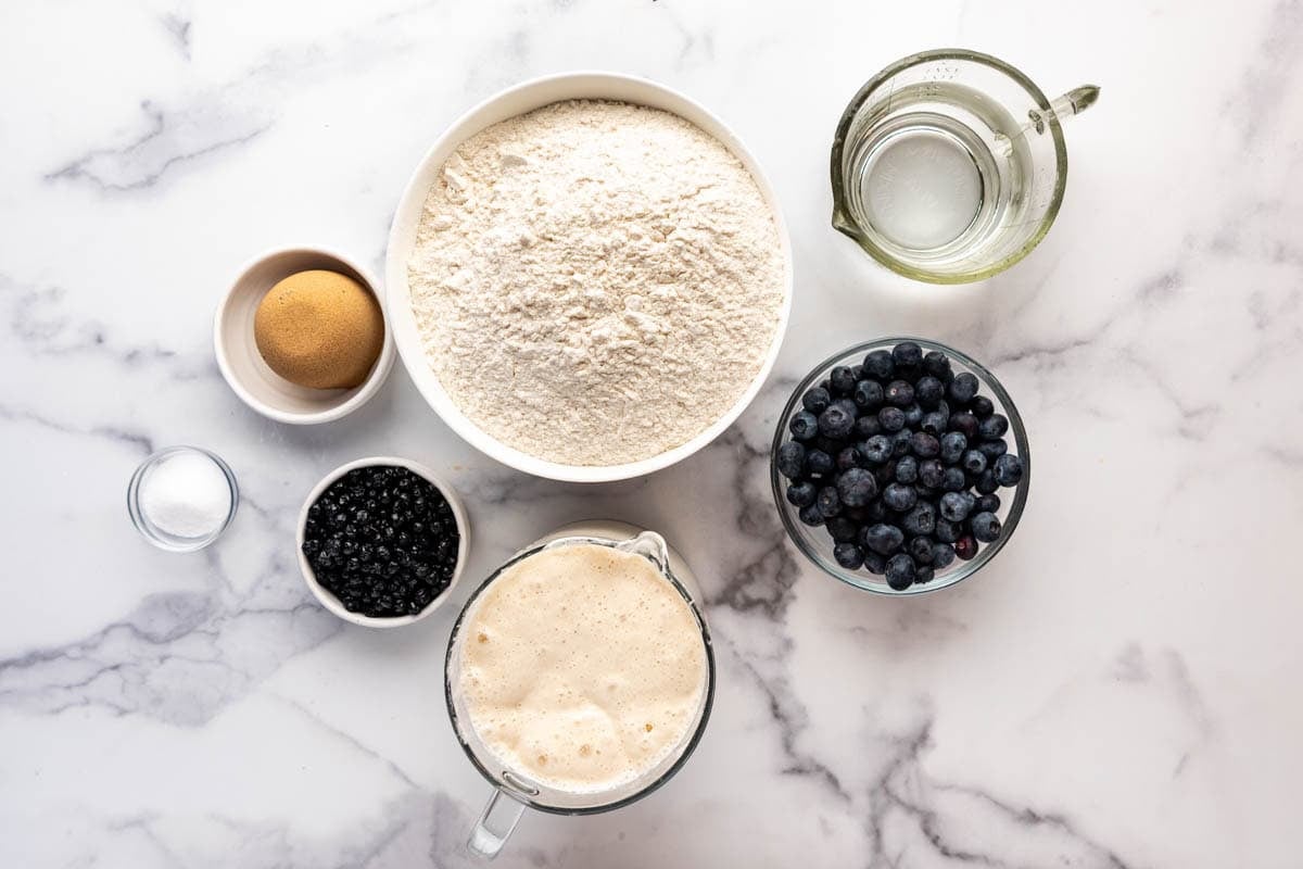 Ingredients for making homemade blueberry sourdough bagels on a white surface.