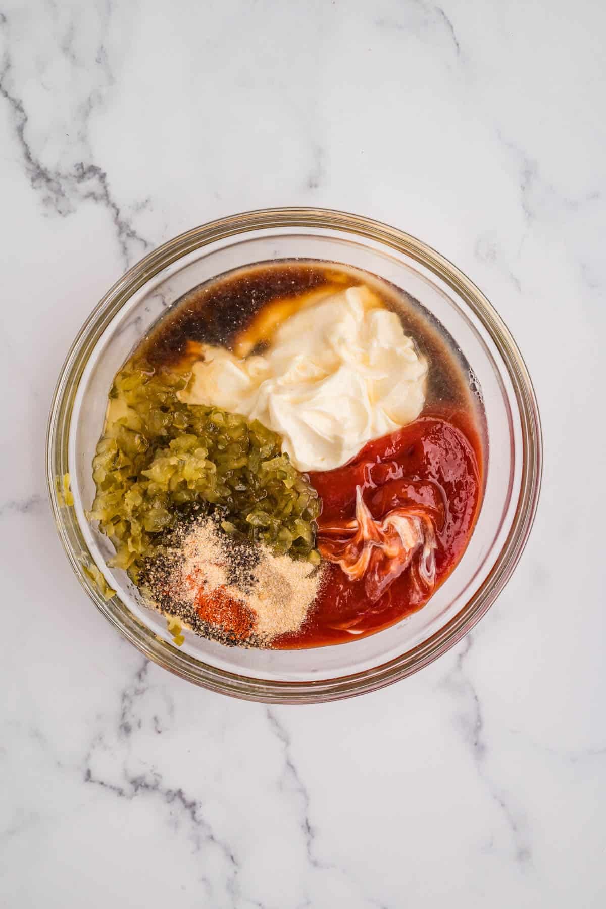 Ingredients like mayo, ketchup, relishes, and spices in a bowl.