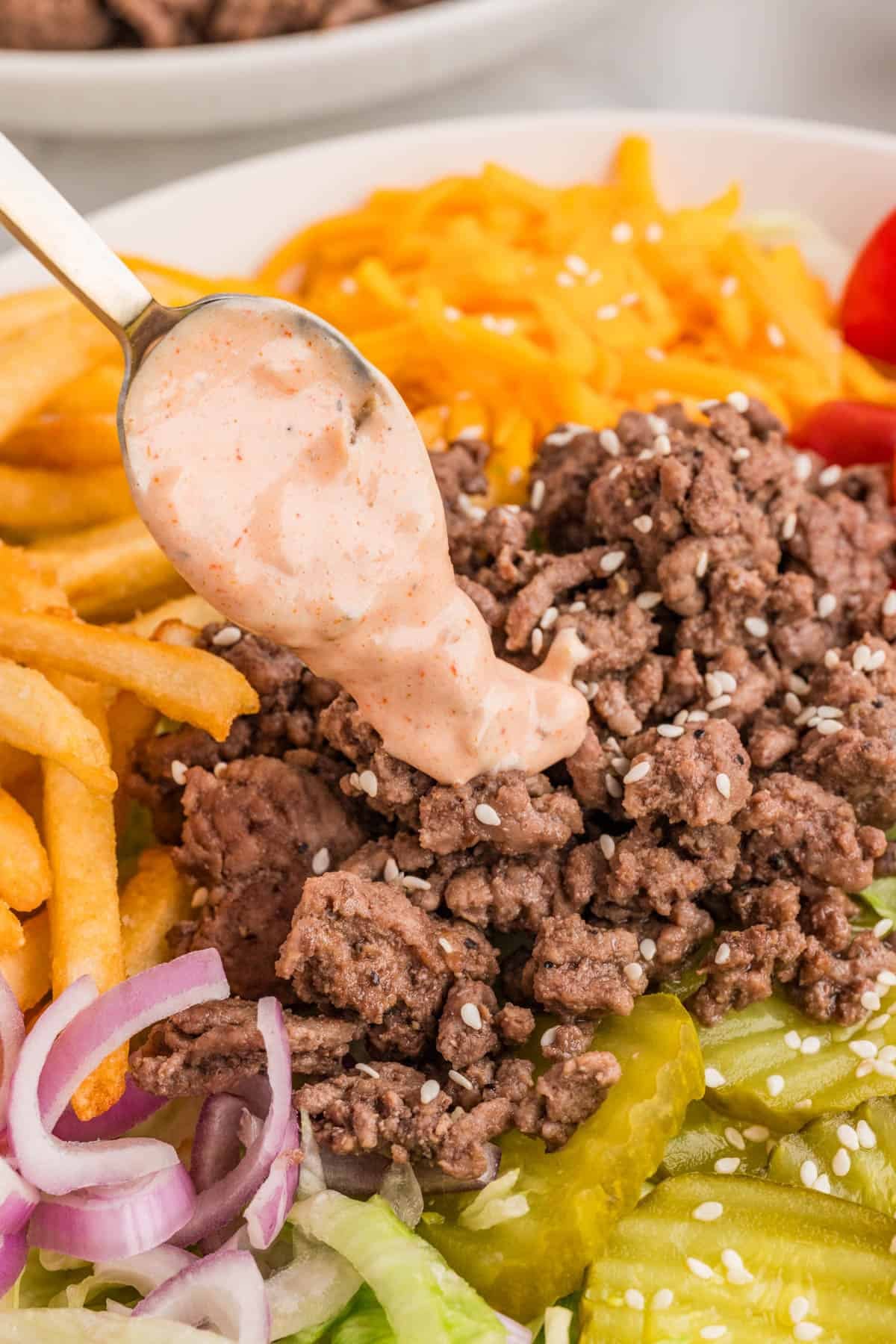 A spoon drizzling burger sauce over browned ground beef in a bowl.
