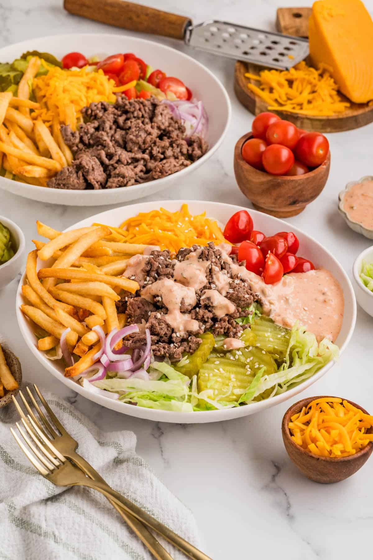 A burger bowl with fries, ground beef, lettuce, tomatoes, and sauce.